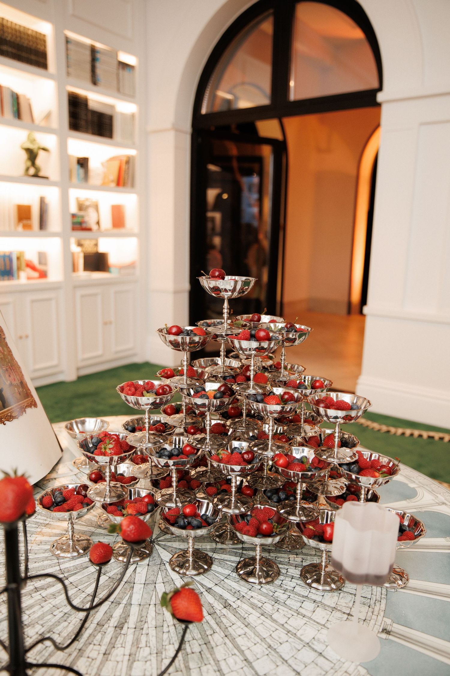 Elegant tiered tower of silver champagne coupes filled with fresh strawberries displayed in a luxurious white interior setting.