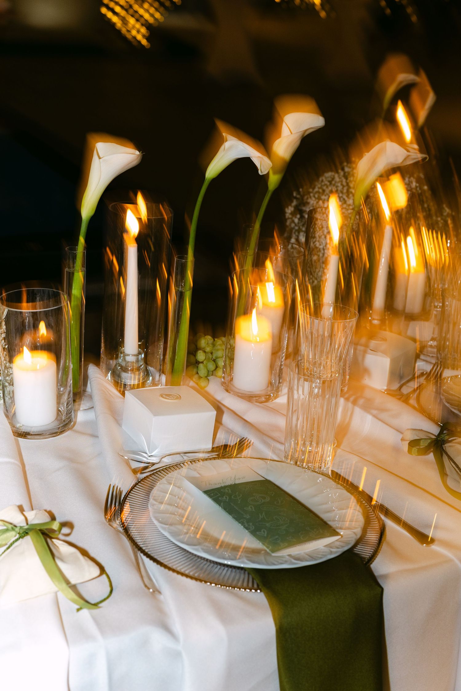 Elegant wedding table setting with white calla lilies and glowing candles.