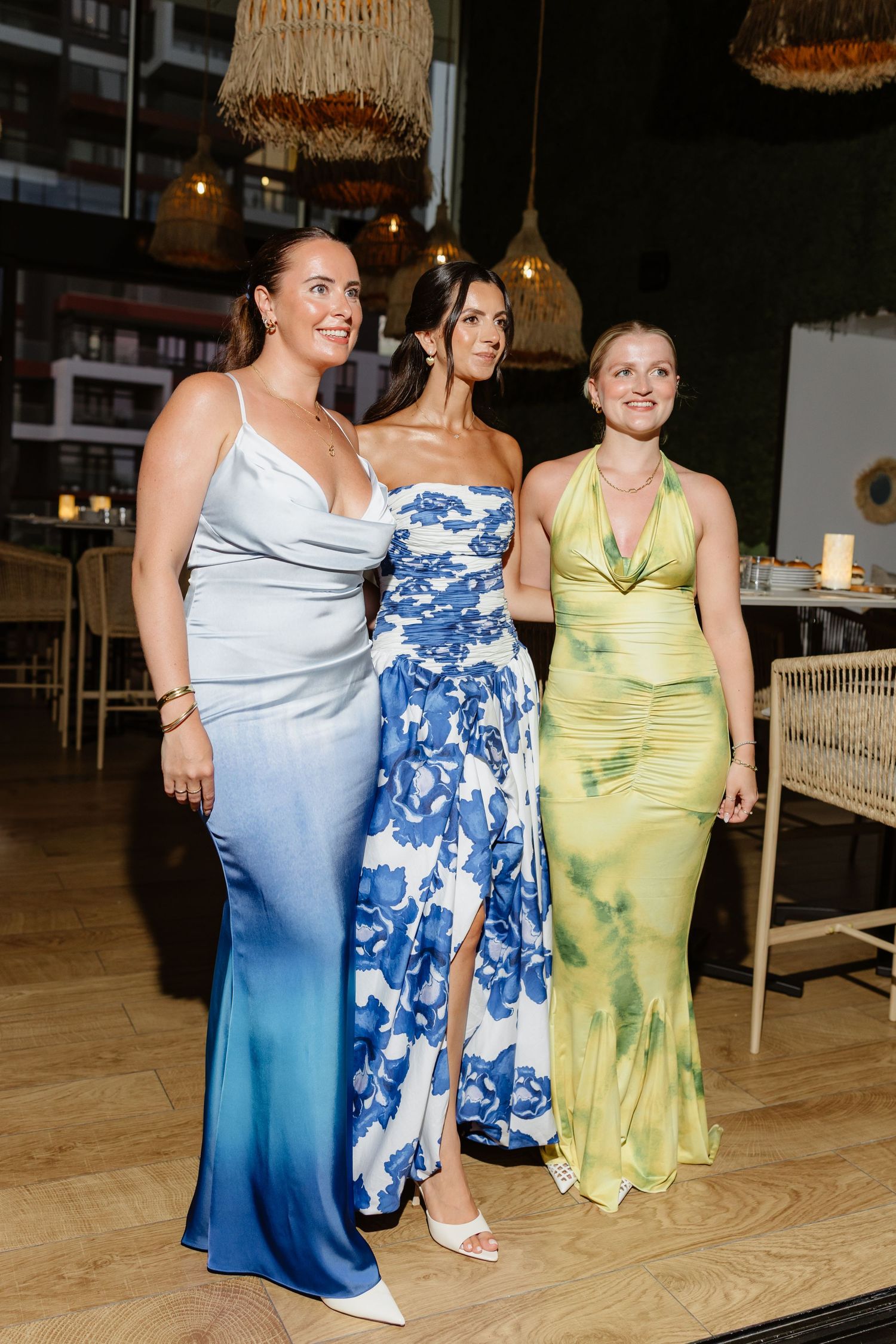 Three women in elegant evening gowns standing together at formal event.