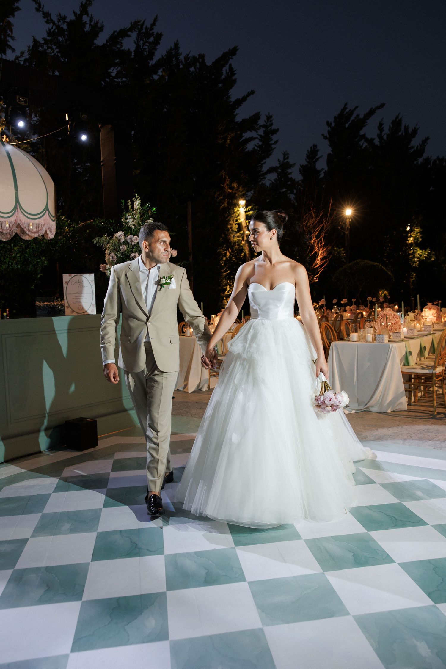 A wedding couple dances on a checkered dance floor at an elegant outdoor evening reception.