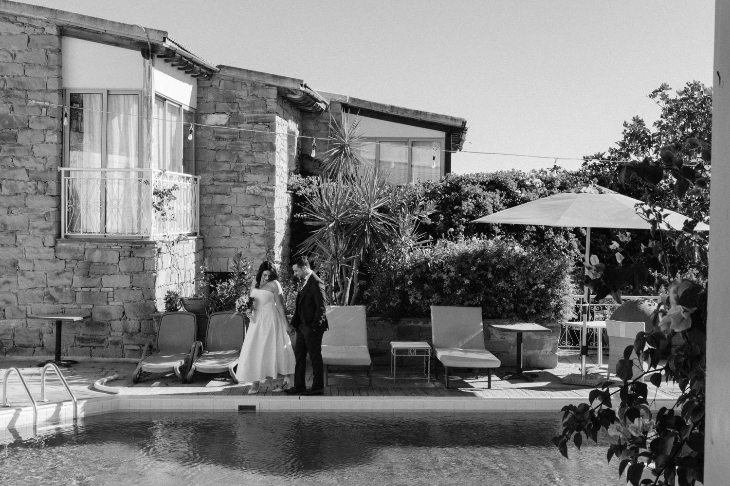 Black and white photo of wedding ceremony by a pool with stone architecture.