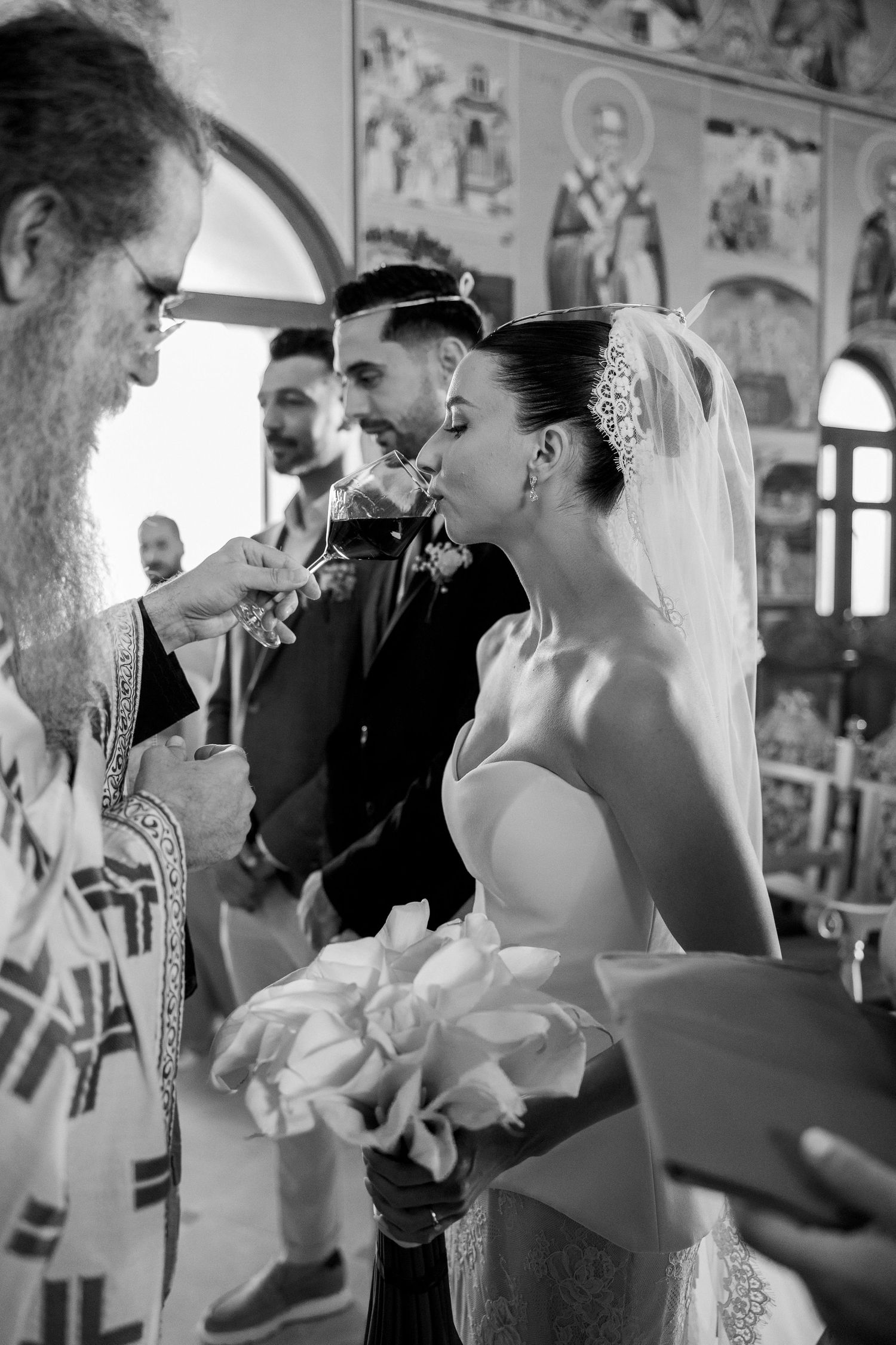Black and white photo of wedding ceremony in an ornate church with religious icons on walls.