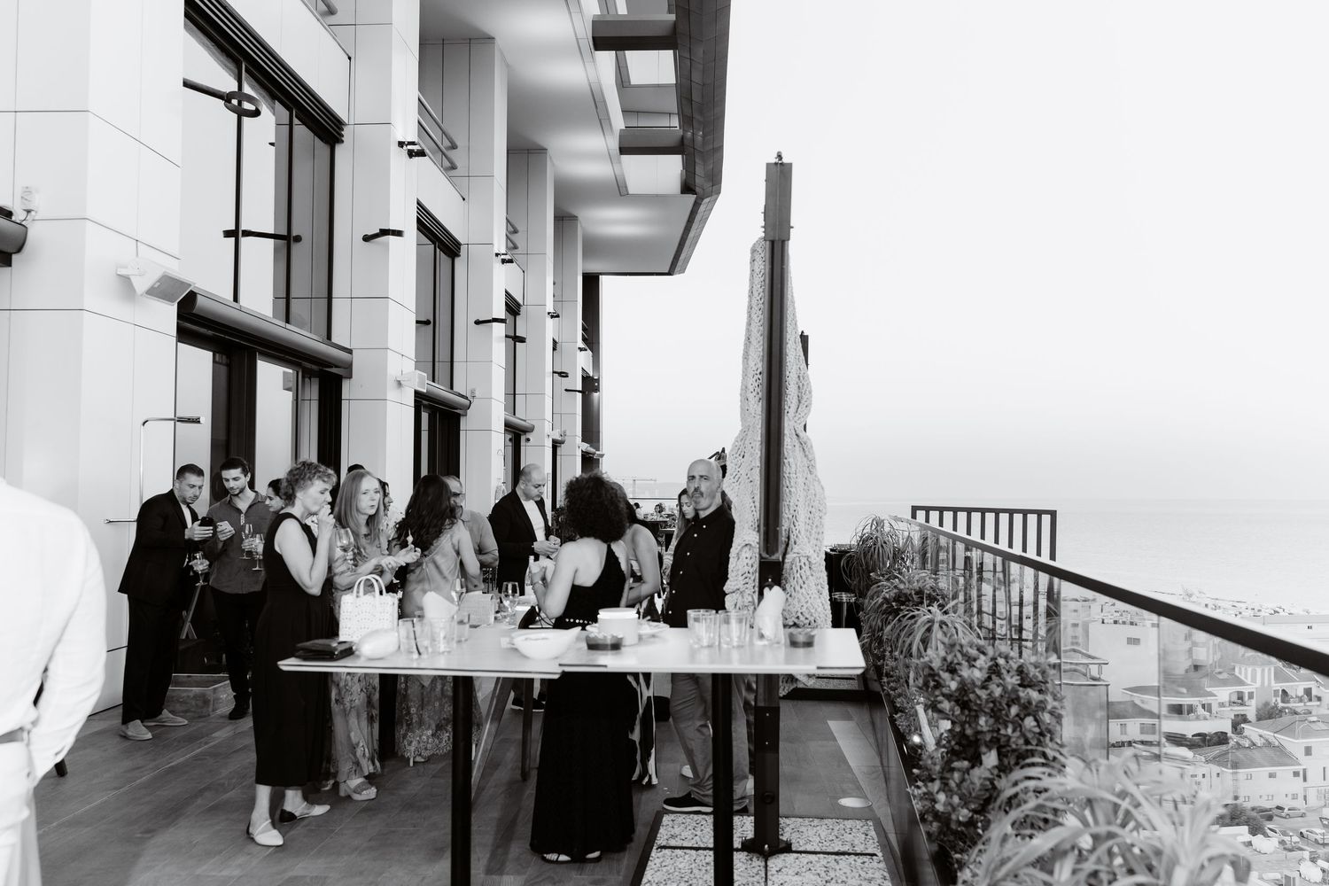 Black and white photo of guests mingling at outdoor rooftop reception.