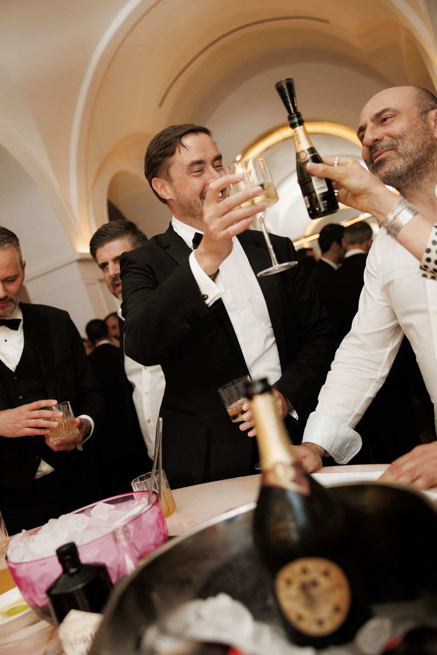 Men in tuxedos toasting with champagne glasses at an elegant formal event.