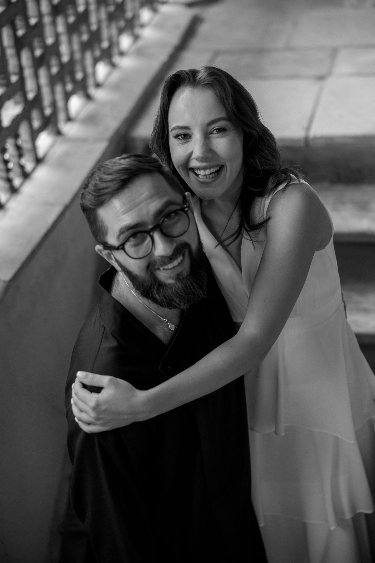 A joyful black and white portrait on a staircase shows an embracing couple.