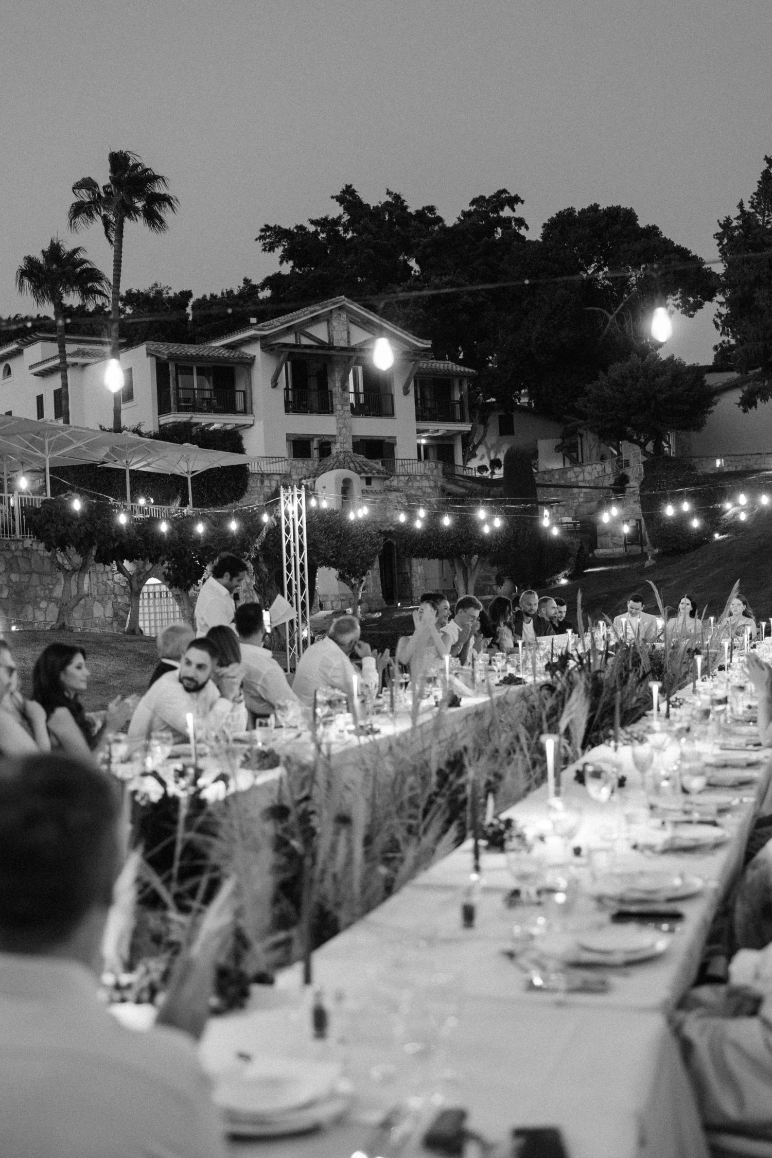Outdoor wedding reception at dusk with long tables, candles, and string lights.