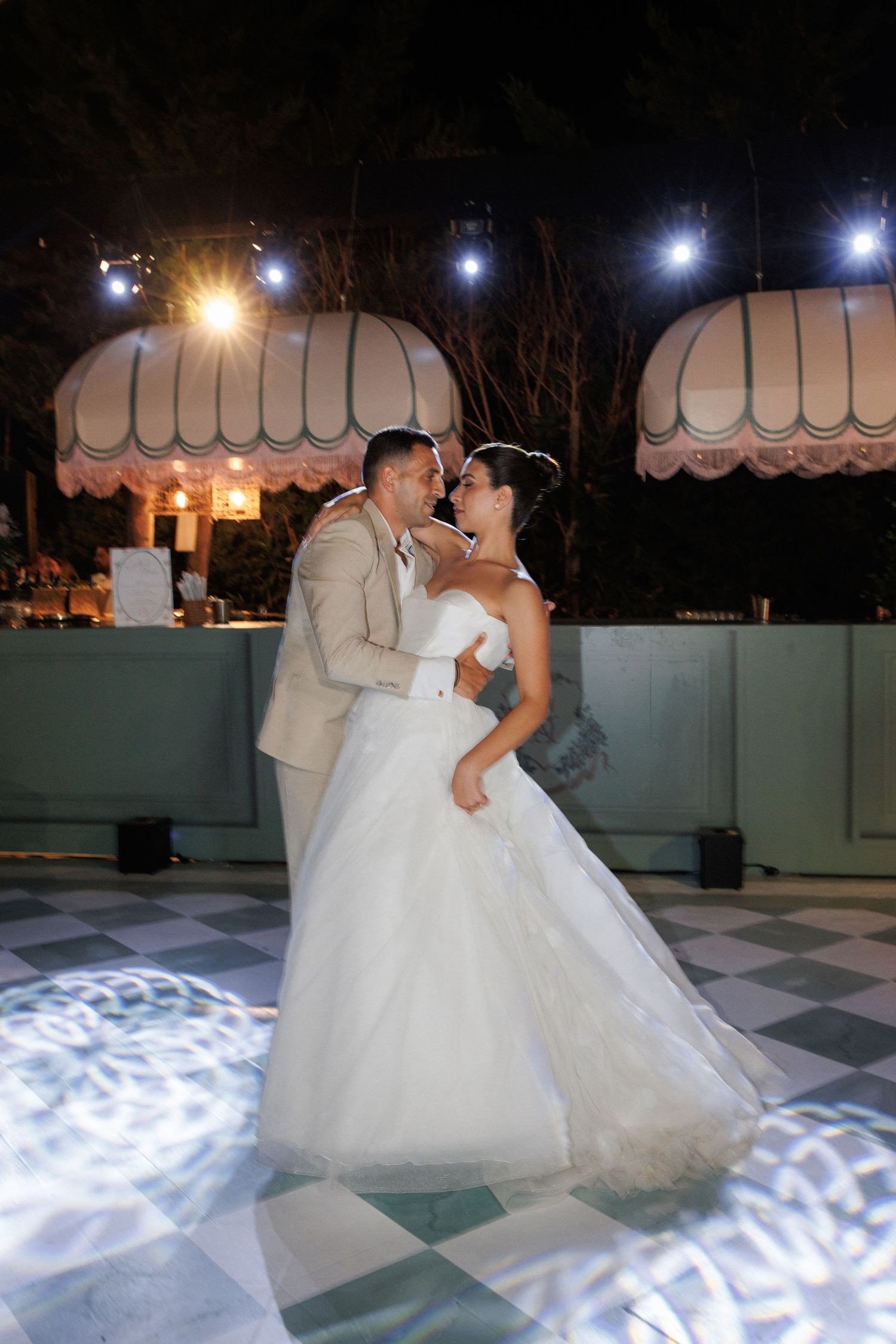 Romantic dance sequence on an illuminated checkered dance floor under elegant white awnings.
