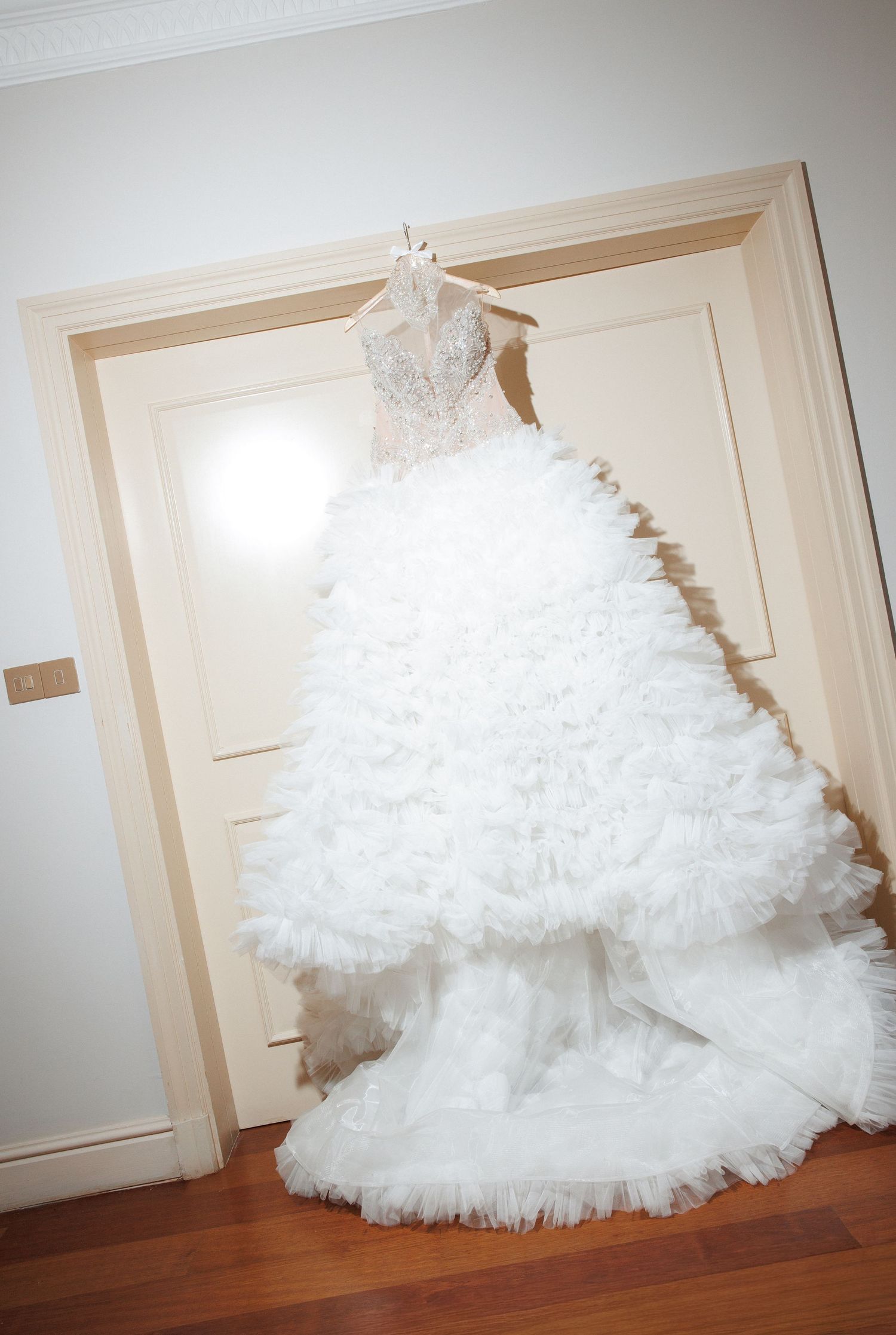 Elegant white ball gown wedding dress with ruffled skirt and beaded bodice hanging on a door.