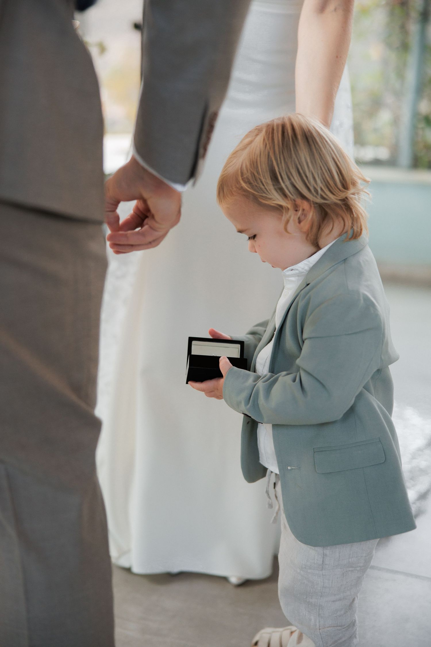 Young ring bearer in light blue suit jacket holding small box during ceremony.