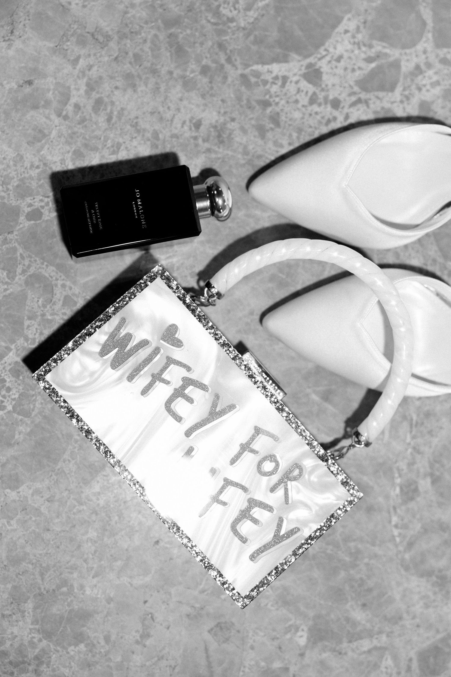 Wedding accessories including white heels and flask with 'Wifey for Life' text on marble surface.