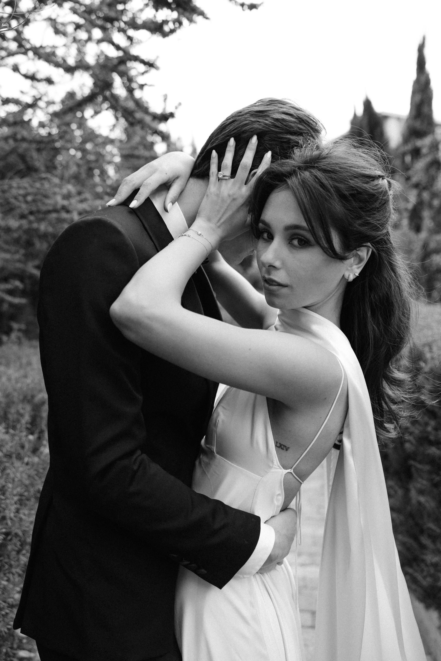 A romantic black and white portrait of a bride and groom embracing outdoors with a flowing veil.