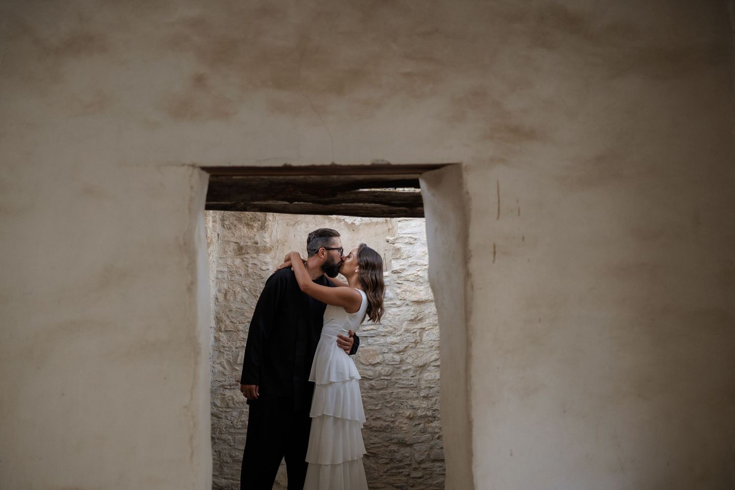 A couple in wedding attire share an intimate moment while standing in a rustic stone doorway.