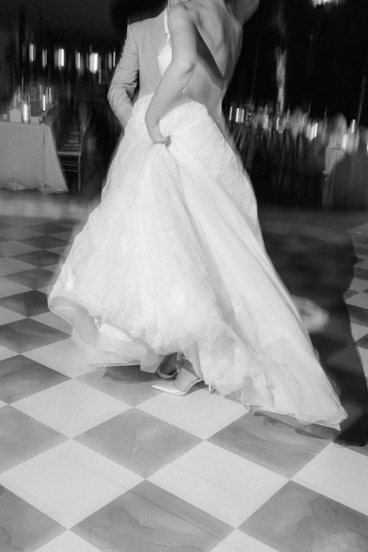A bride's flowing white dress swirls across a checkered dance floor in black and white.