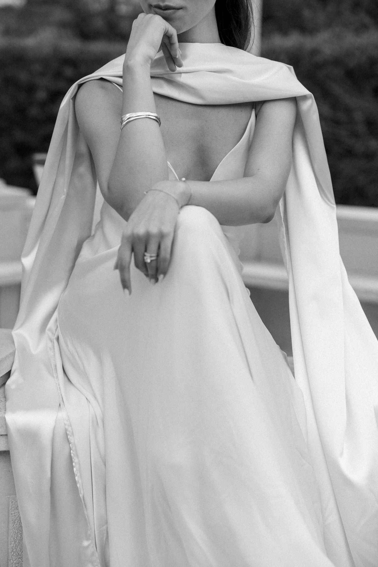Elegant black and white photograph of a bridal gown with flowing sleeves and delicate details, highlighting its graceful silhouette.