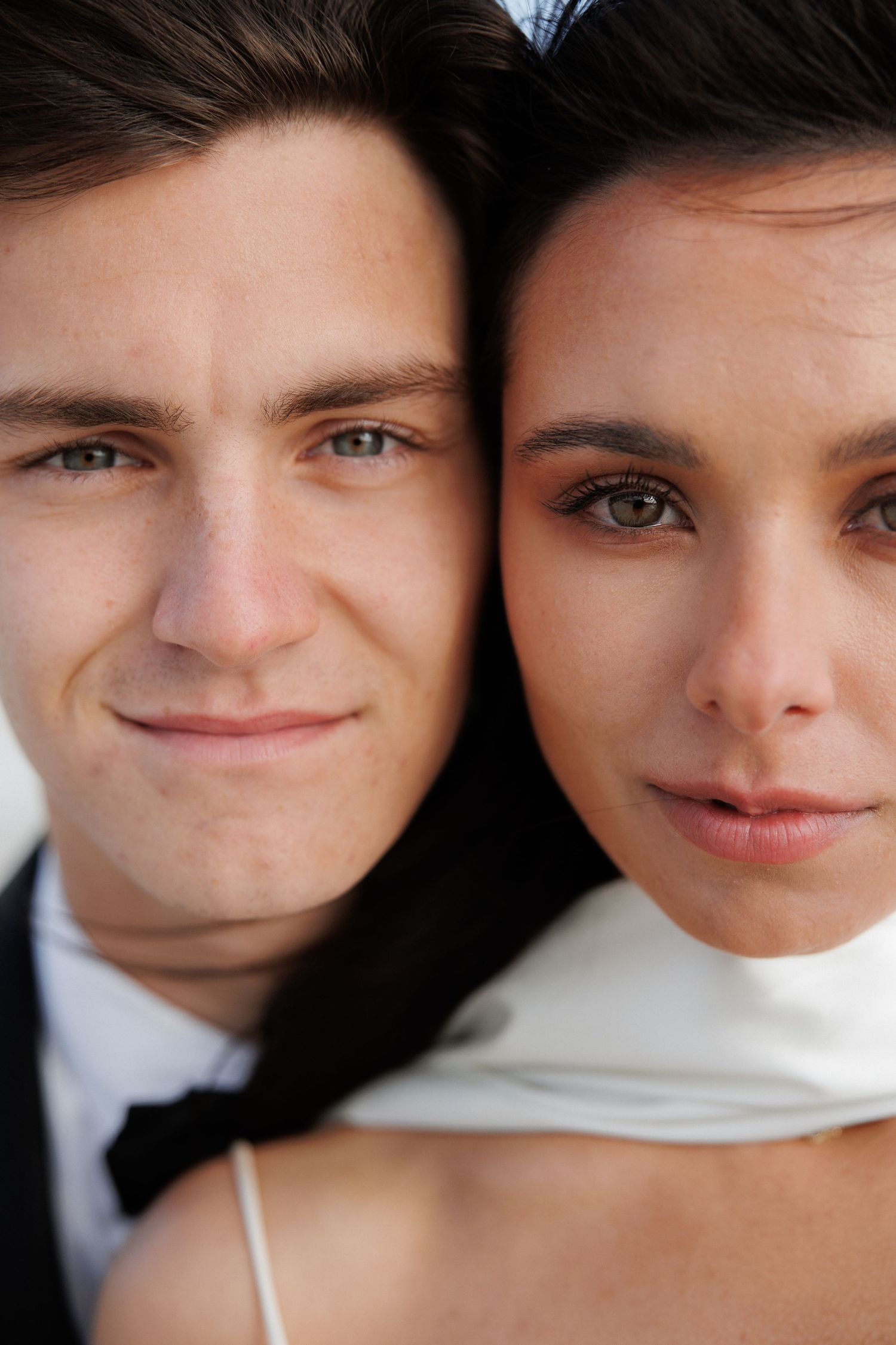 Close-up portrait of a couple in wedding attire with dark hair looking at camera, smiling warmly.