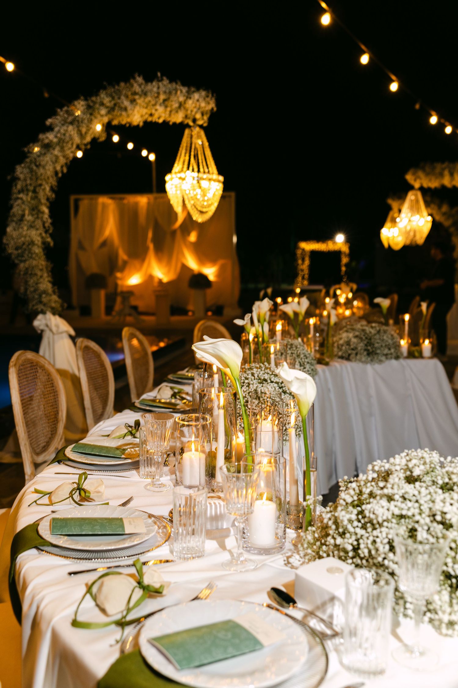 Wedding reception tables with white linens, greenery, and warm glowing string lights overhead.