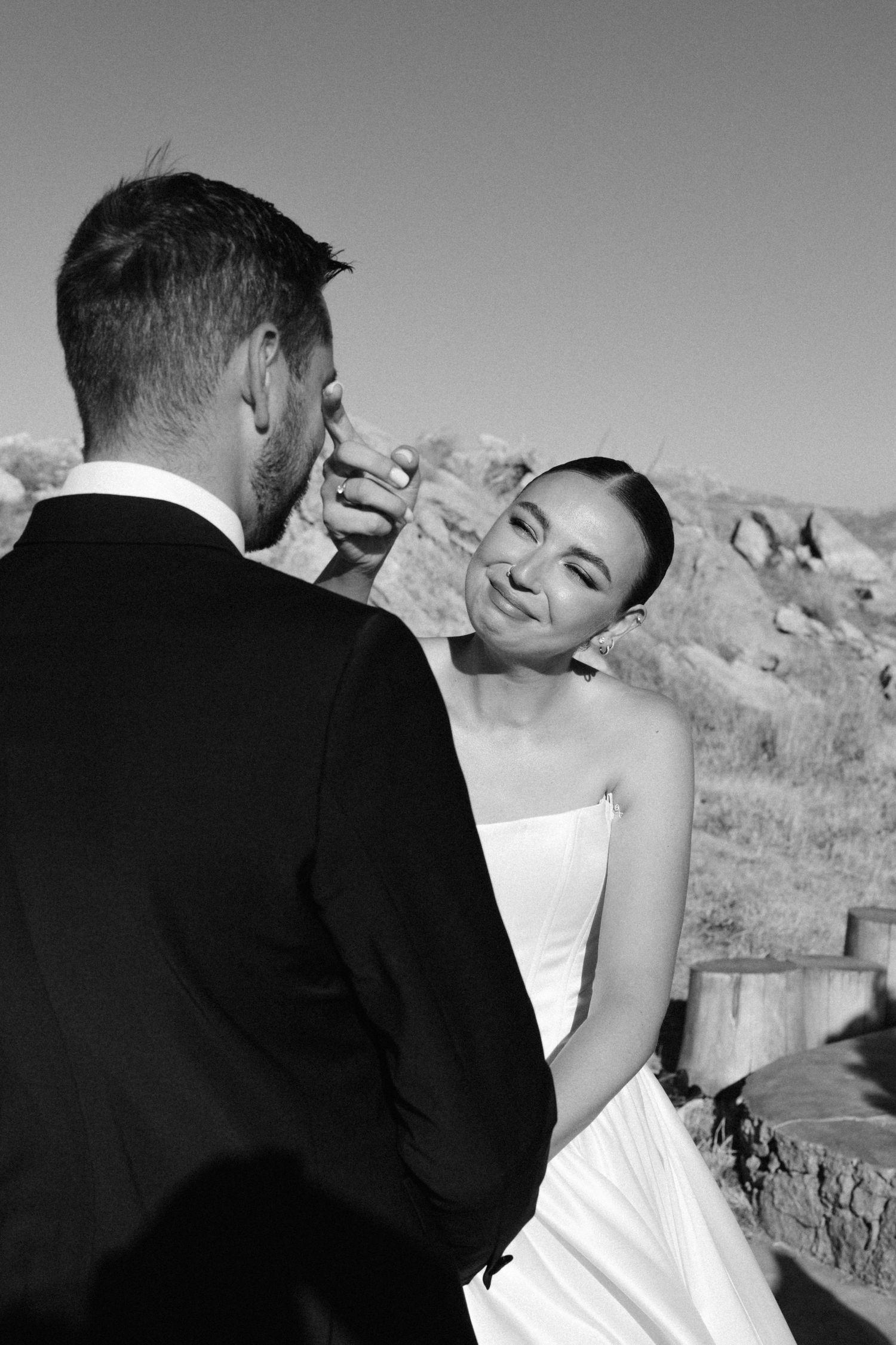 Black and white wedding photo of bride touching grooms face outdoors with rocky landscape background.