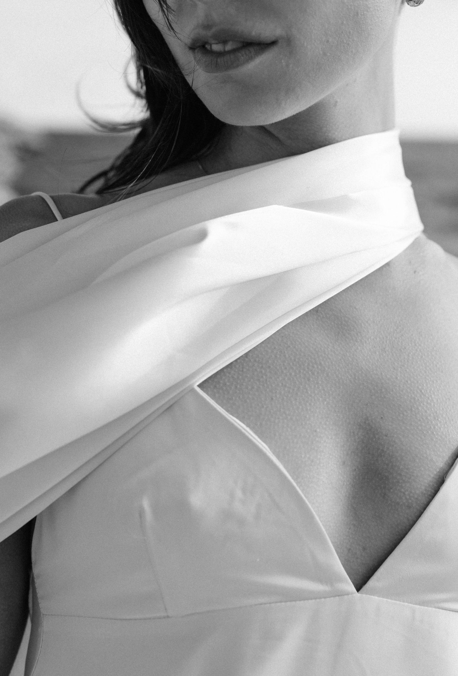 Black and white close-up photograph showing flowing white fabric draped across shoulders in an elegant formal style.