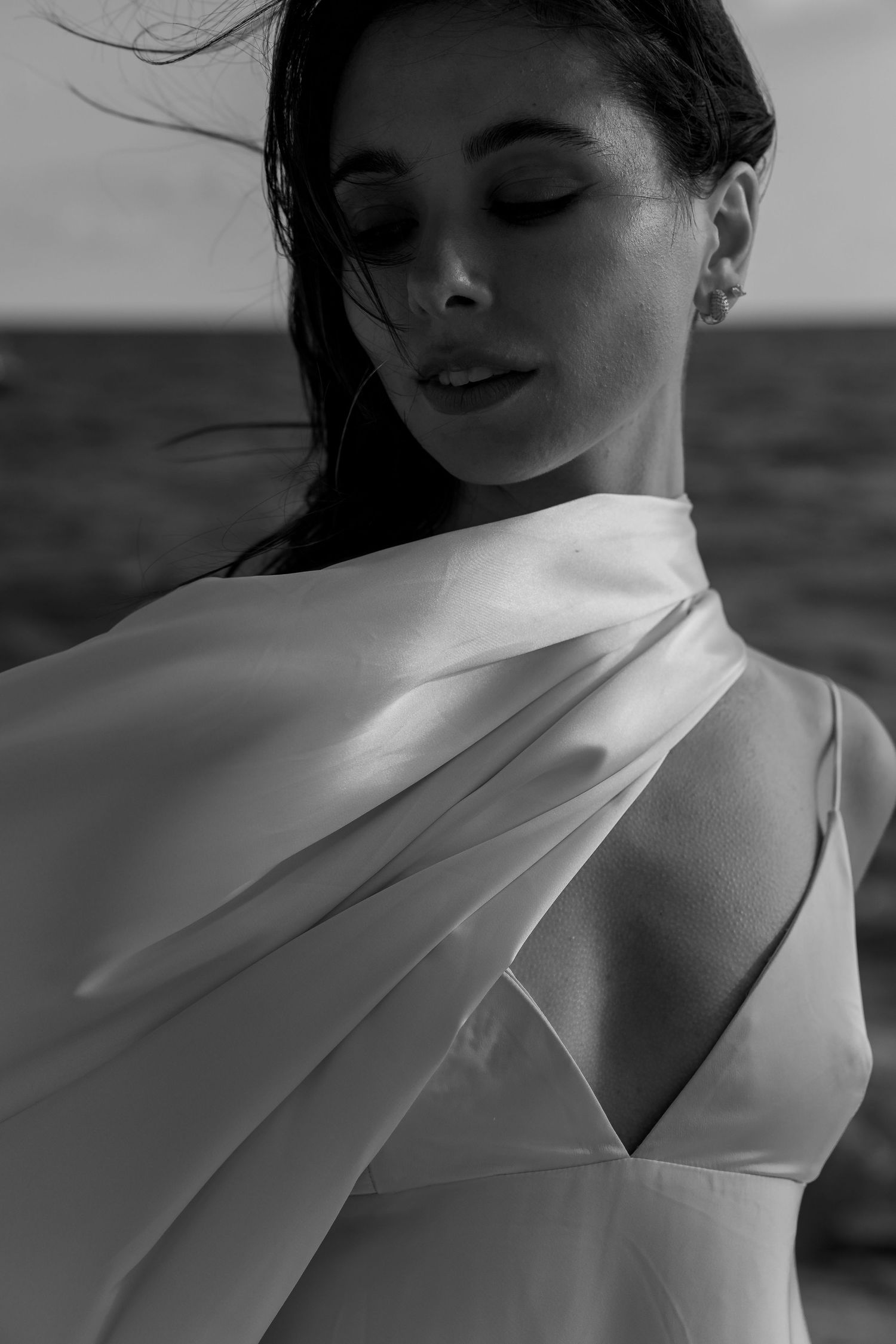 Artistic black and white portrait of a figure in billowing white fabric against a dark background.