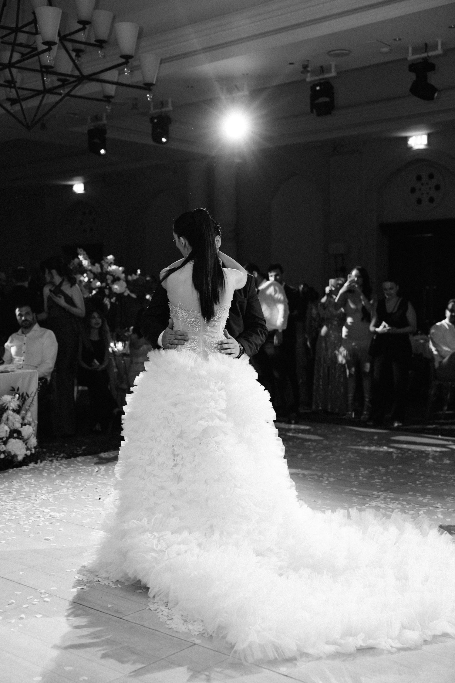 Black and white photo of a bride in a ruffled ball gown dancing with groom at elegant wedding reception.