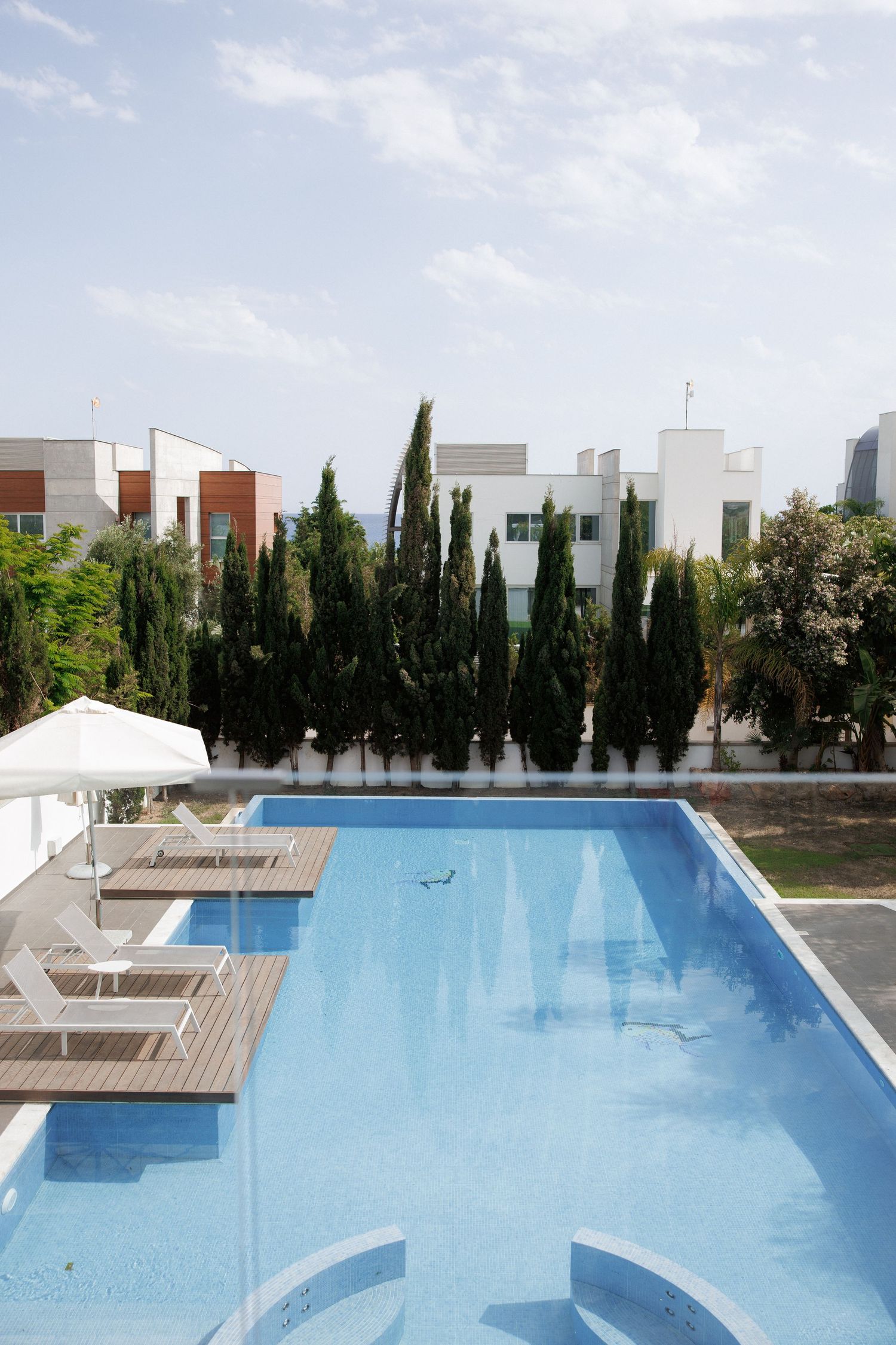 Modern swimming pool surrounded by cypress trees and lounge chairs at a luxury resort.