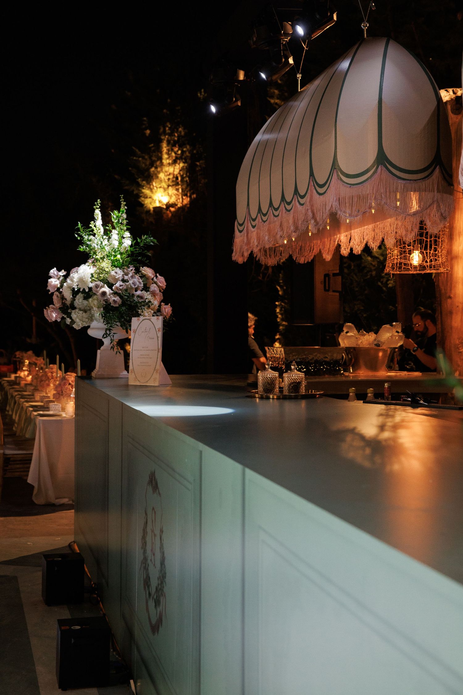 Elegant wedding reception setup with white floral arrangements and scalloped awnings illuminated by warm lighting.