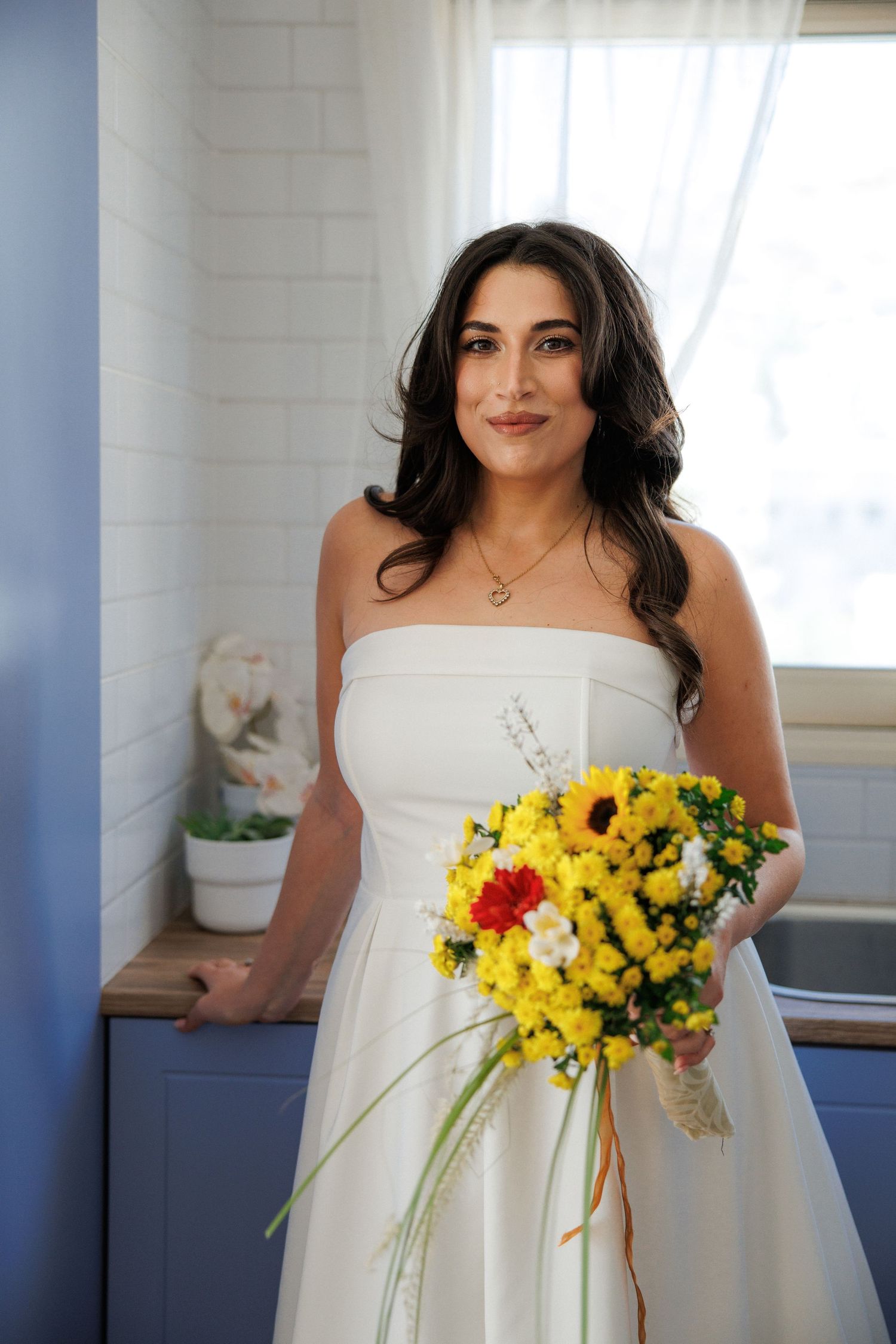 A bouquet of bright yellow sunflowers and wildflowers complements a white strapless wedding dress.