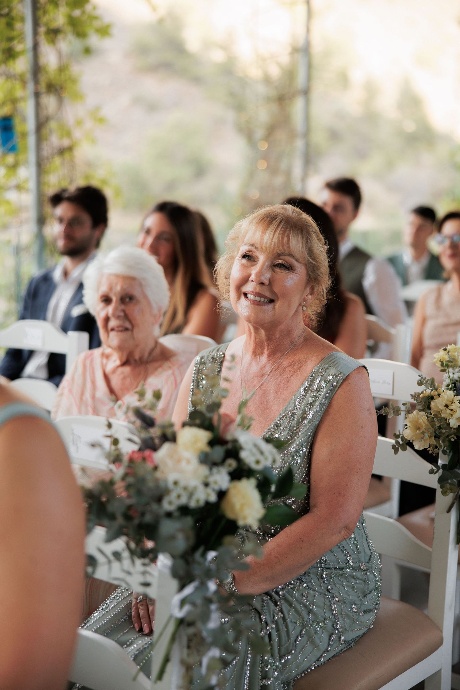 Guests enjoying an elegant outdoor wedding reception with floral centerpieces and white chairs.
