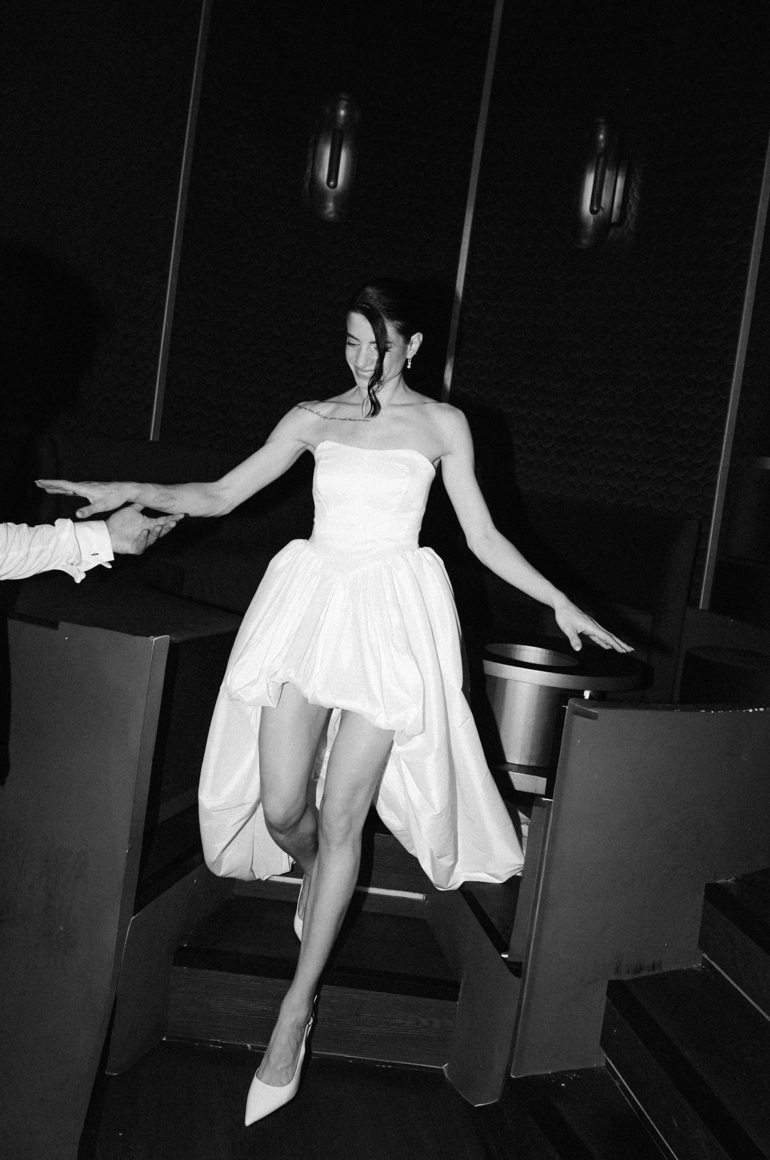 Woman in white strapless mini dress and heels descending stairs in black and white photo.