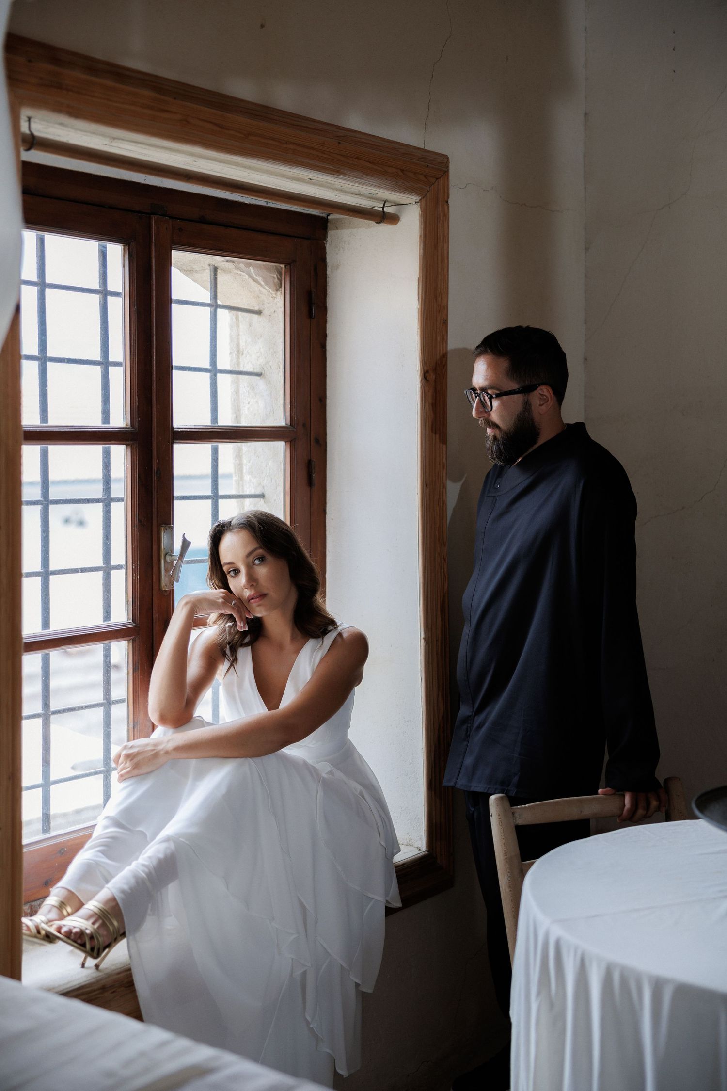 Artistic black and white photo series showing a couple in white and black attire by a window in intimate poses.