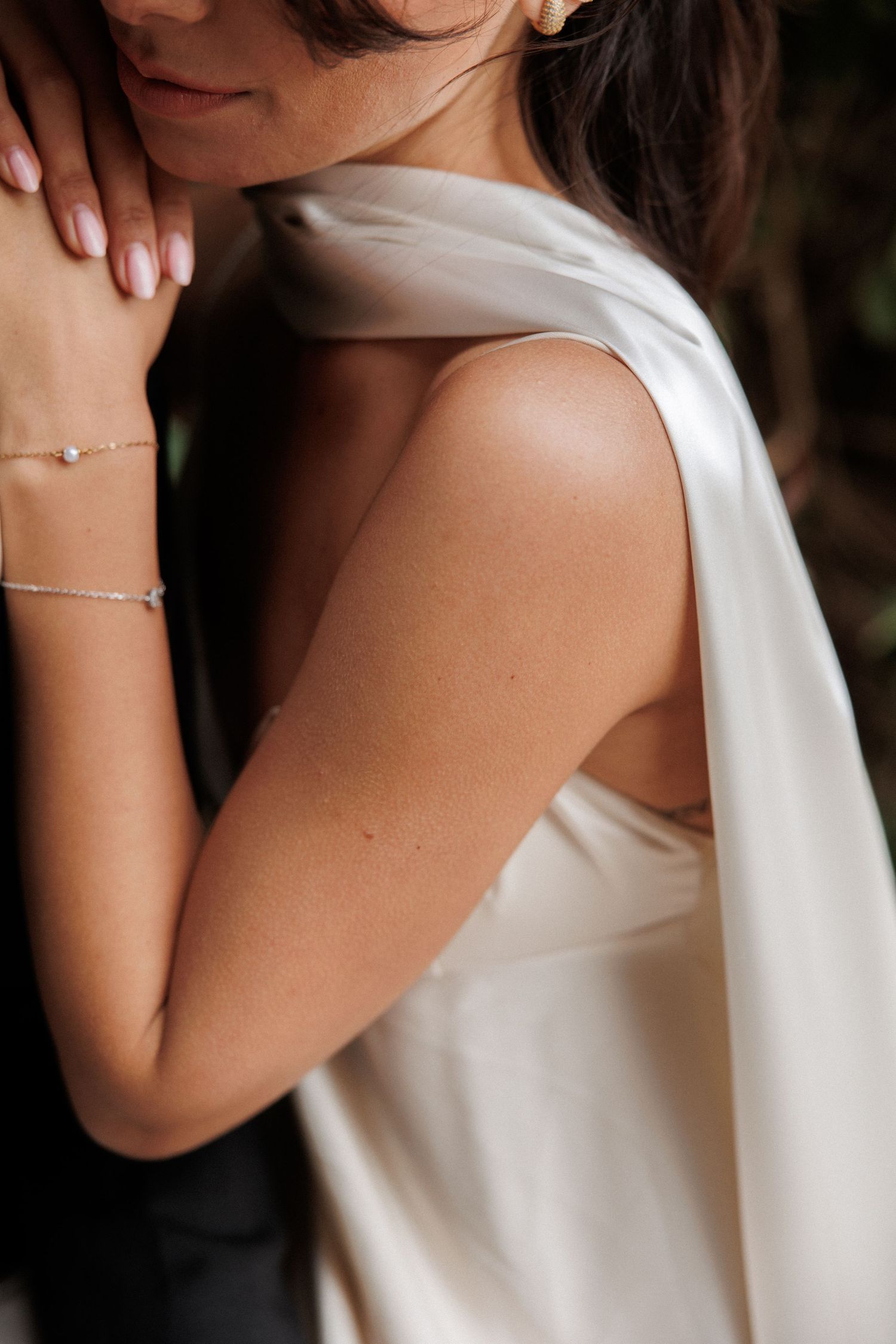 Close-up shot of someone wearing a white sleeveless dress with delicate gold bracelets on their wrist.