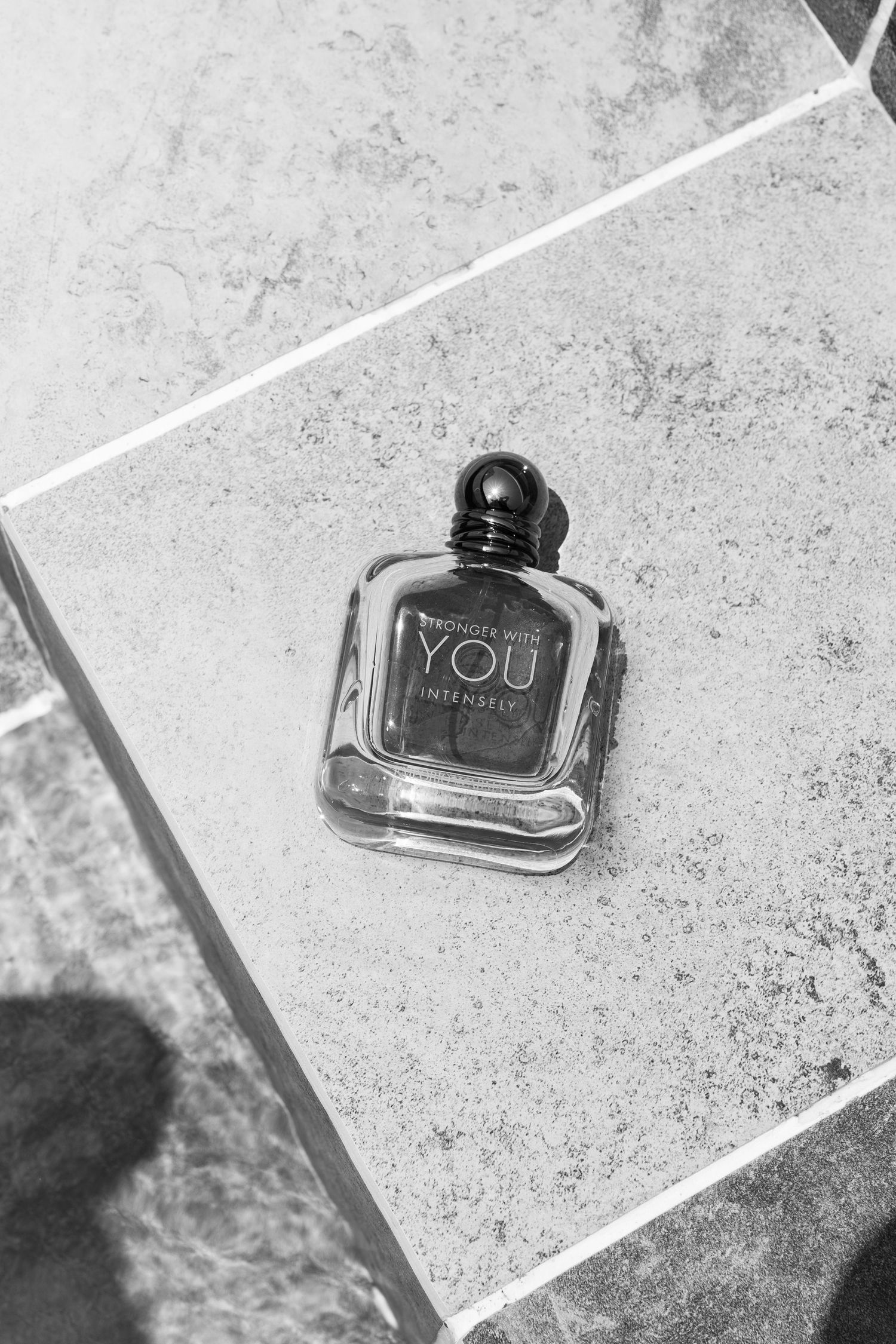 Black glass ink bottles on a white textured surface cast diagonal shadows in a minimalist composition.