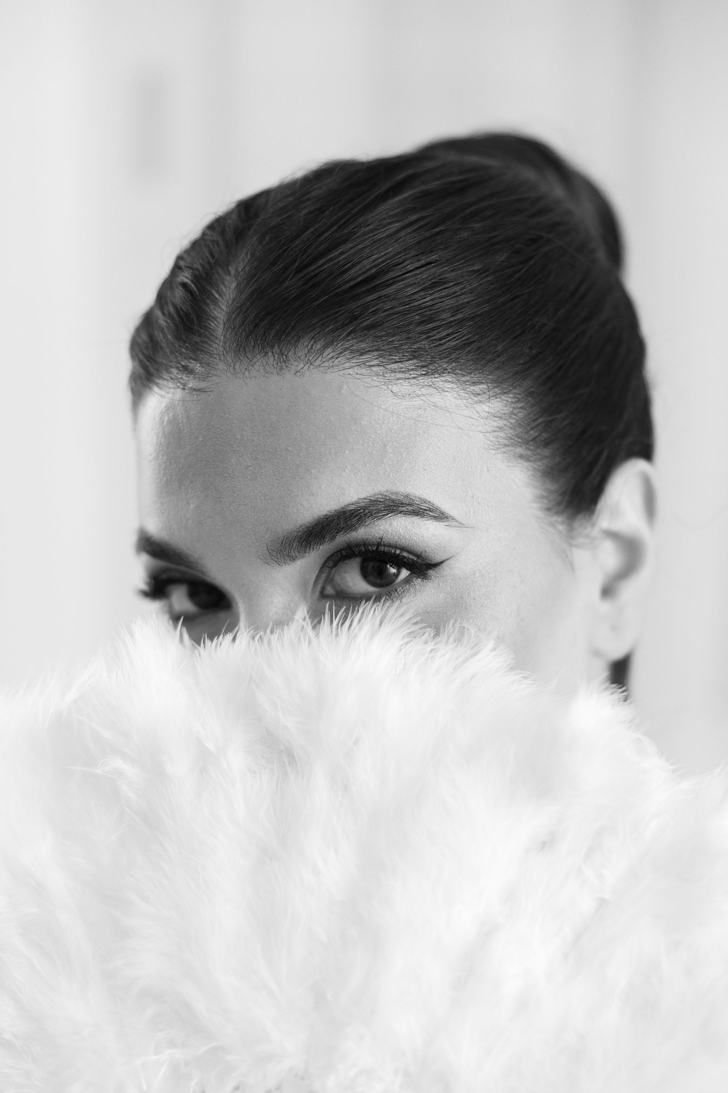 Close up view of eyes and eyebrows against a white background with feathers in the foreground.