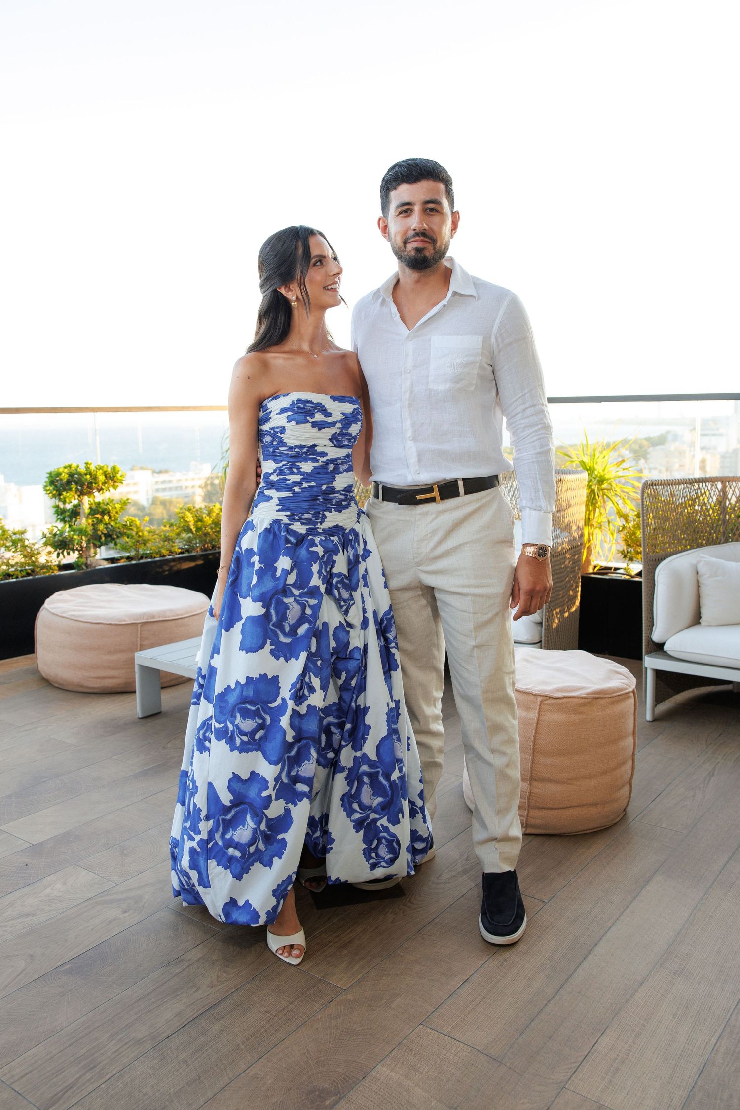 Couple poses on outdoor terrace wearing coordinated blue and white summer formal attire.