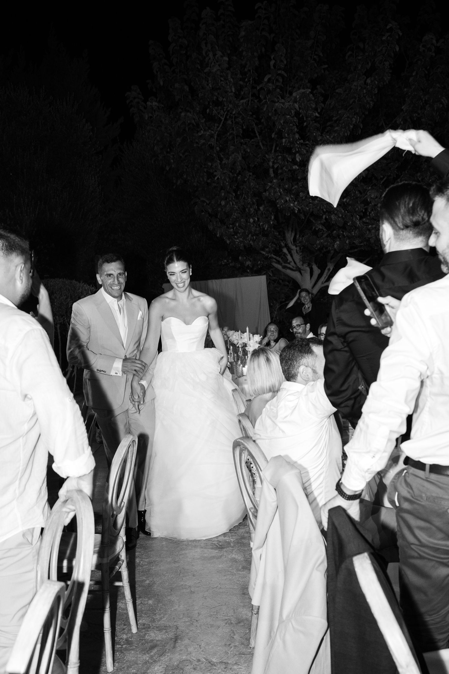 People in formal attire dancing and socializing at an outdoor evening event in black and white photography.