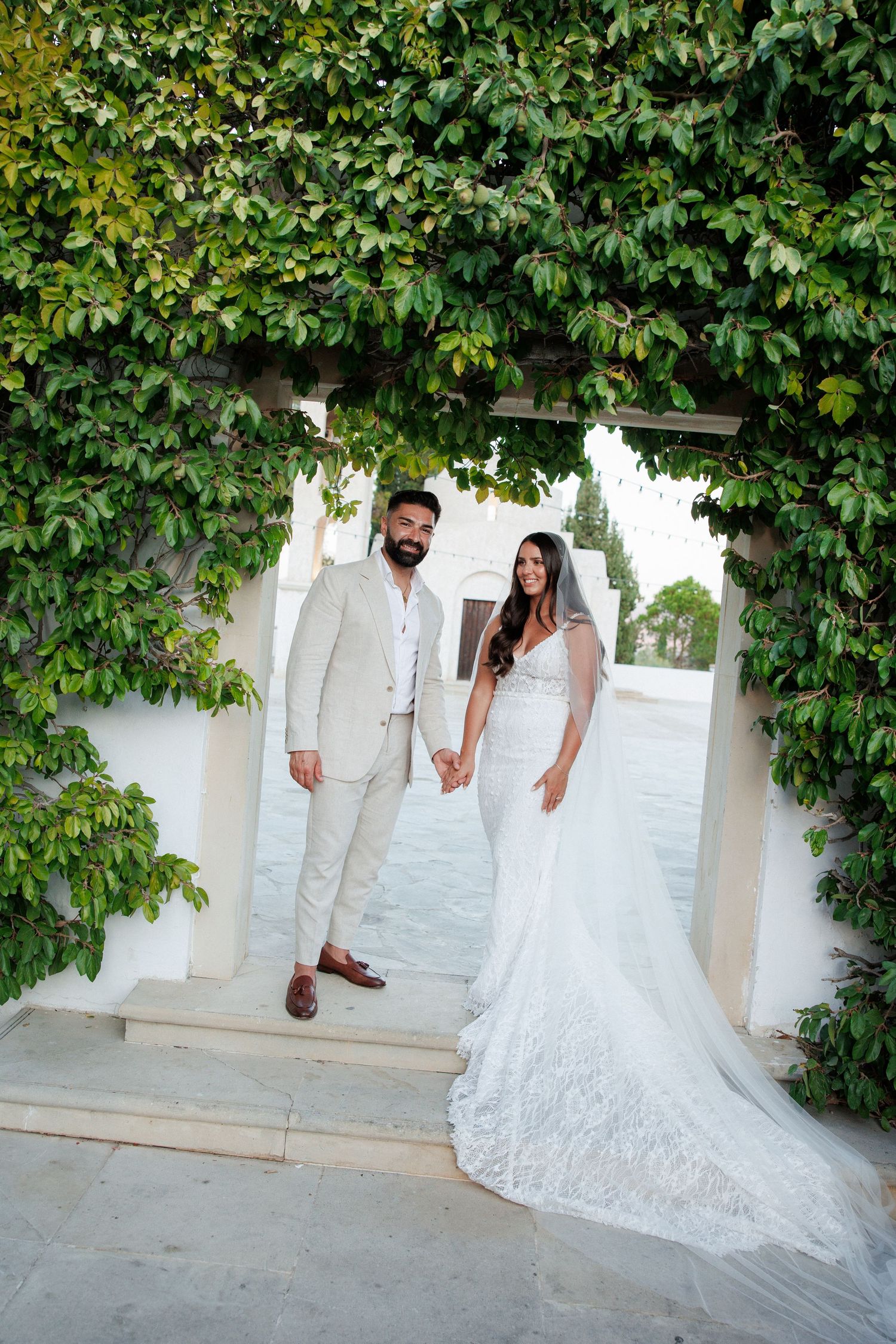 Bride and groom hold hands under a lush green ivy archway at an elegant outdoor wedding venue.