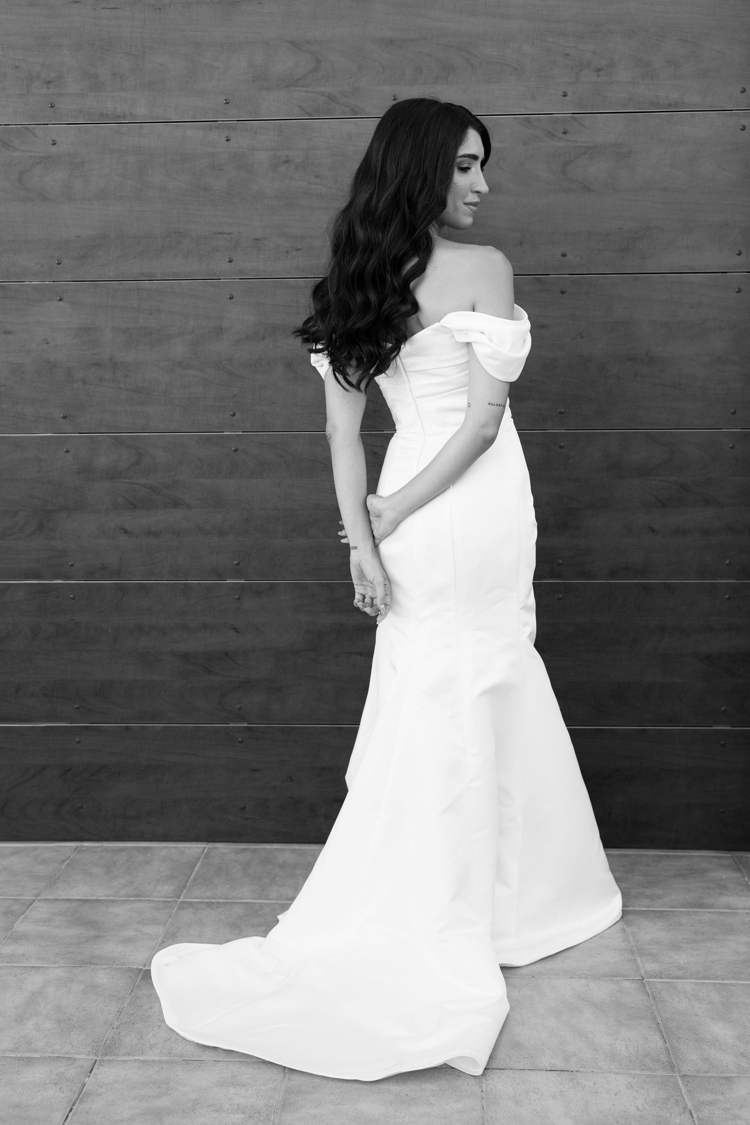 Bride in off-shoulder white mermaid wedding gown posing elegantly in black and white photo.