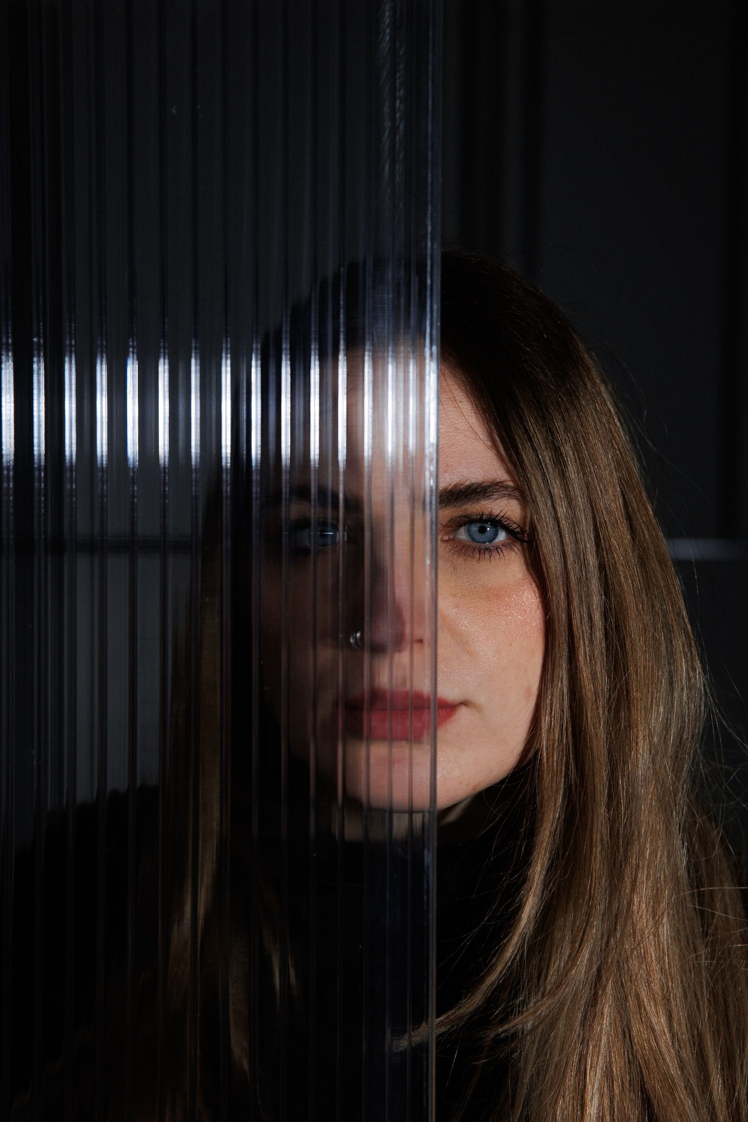 Artistic portrait through glass showing dramatic lighting and reflections.