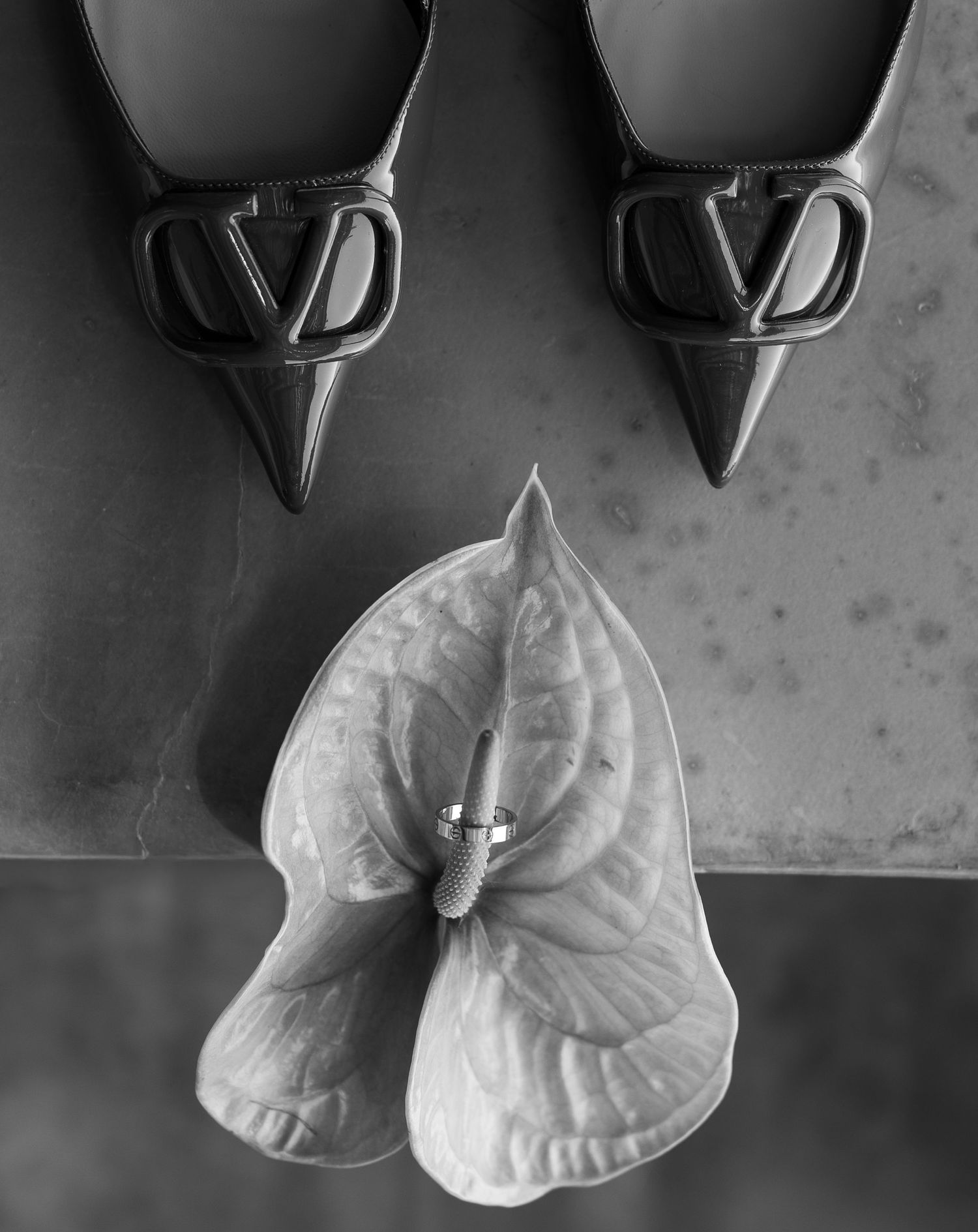 Black and white photo of Valentino VLogo heels beside an anthurium flower with a diamond ring resting on it.