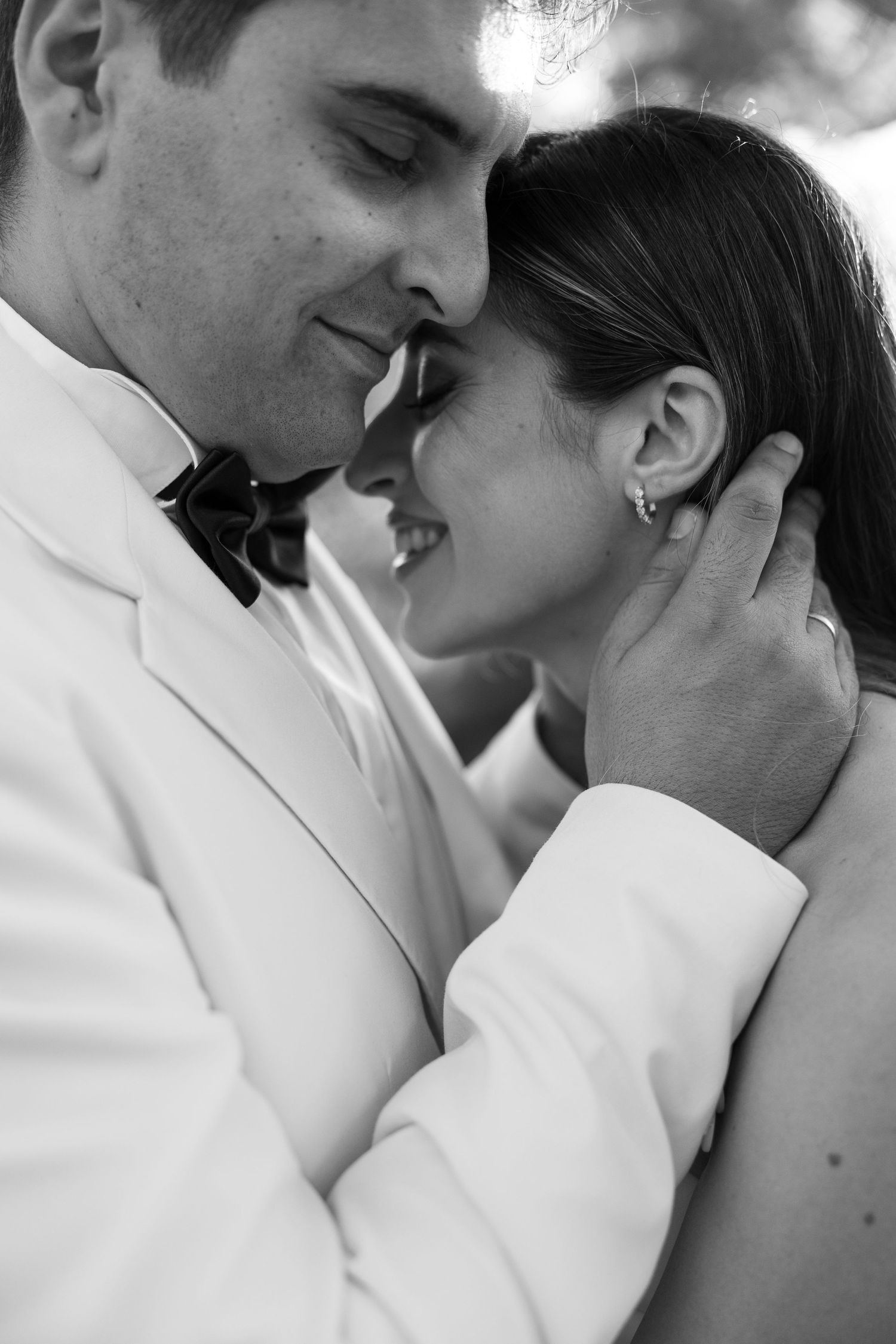 Black and white photo of a bride and groom sharing an intimate moment, groom in white tuxedo gently holding her face.