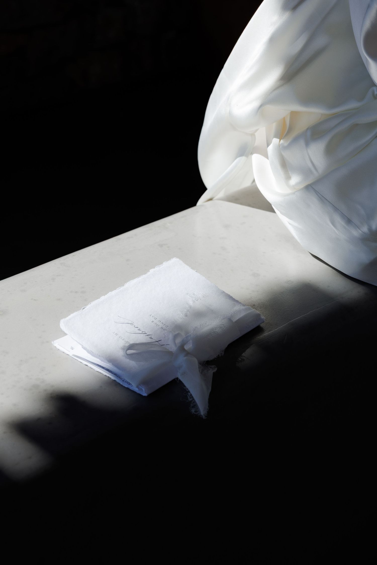 White fabric and folded papers resting on a marble surface in dramatic chiaroscuro lighting.