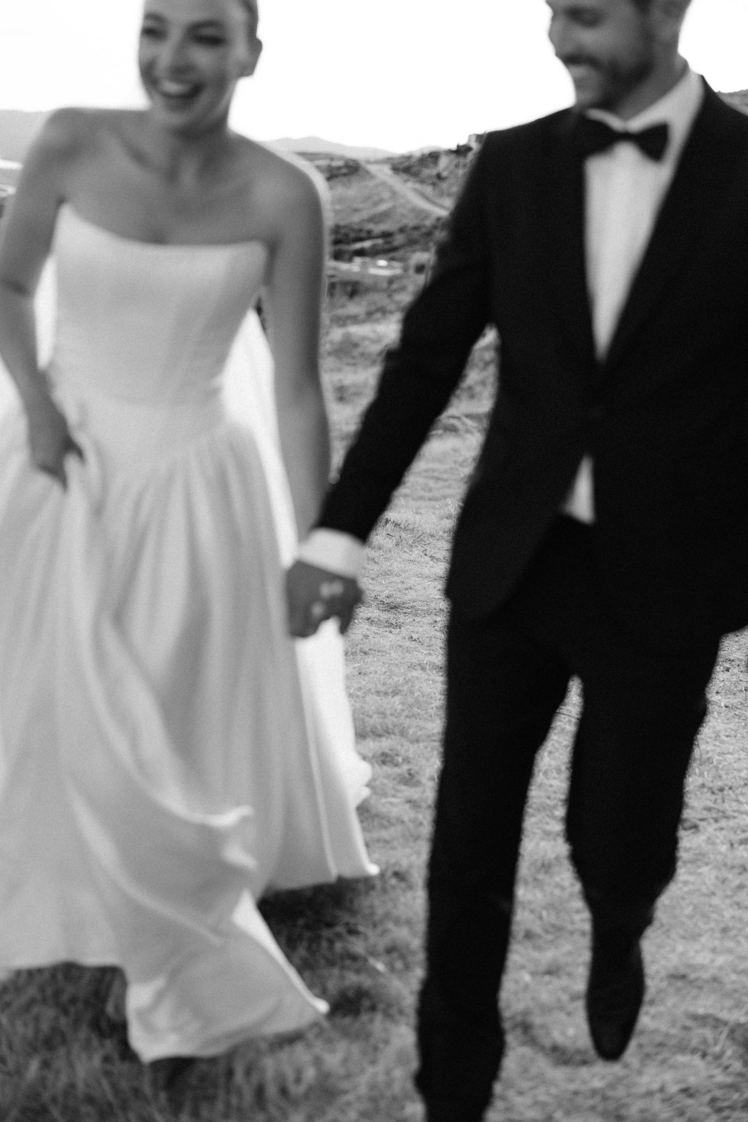 Black and white photo of smiling bride and groom holding hands walking outdoors on their wedding day.