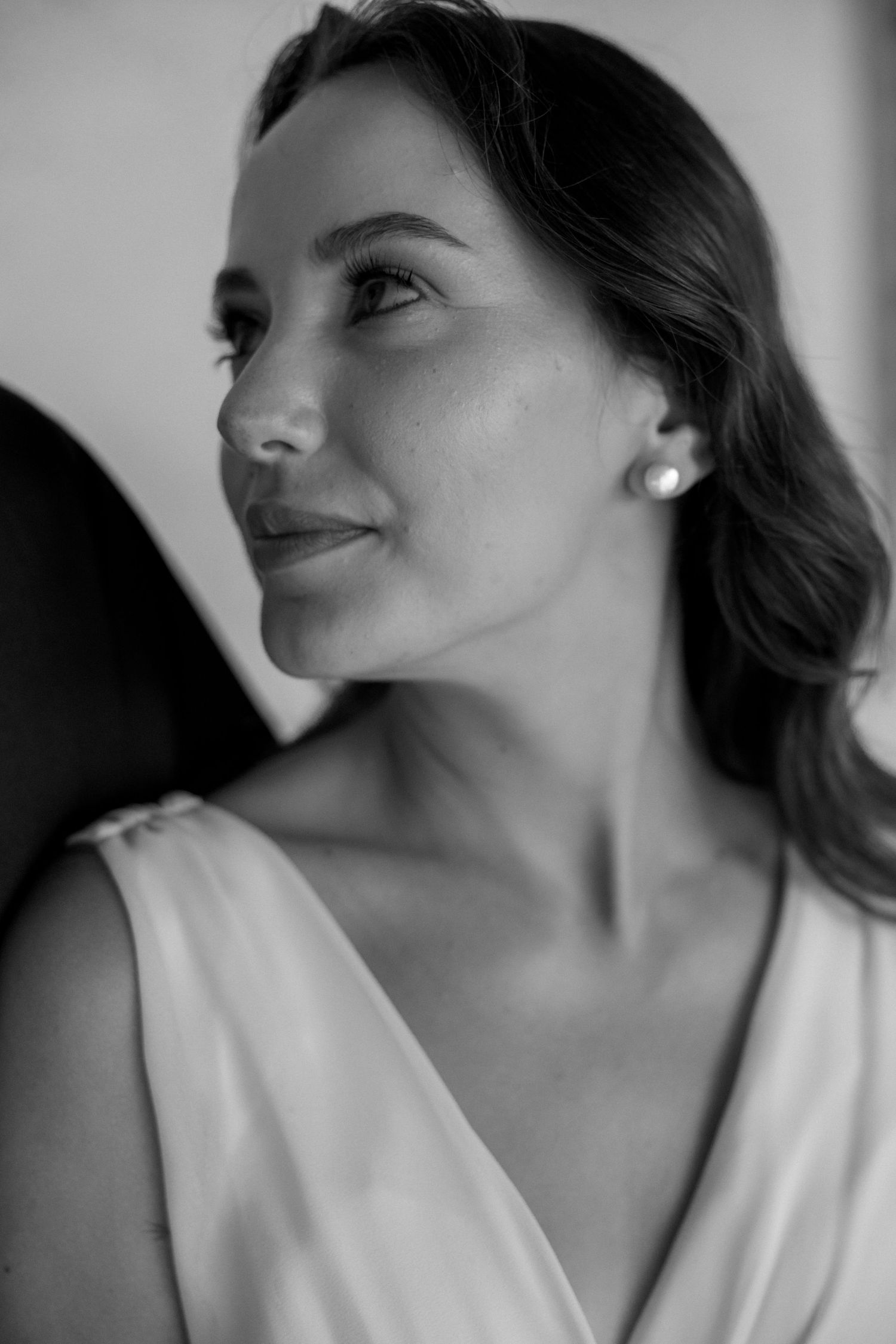 Black and white portrait of a woman in a white dress looking to the side with a soft smile and pearl earring.