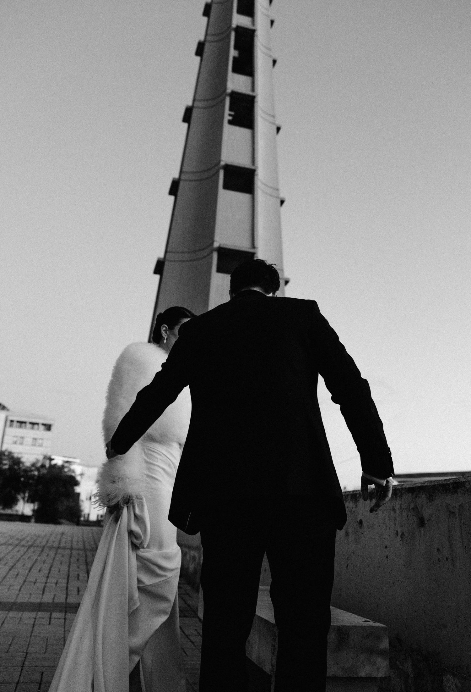 Black and white silhouette of bride and groom walking toward a tall tower at dusk on their wedding day.