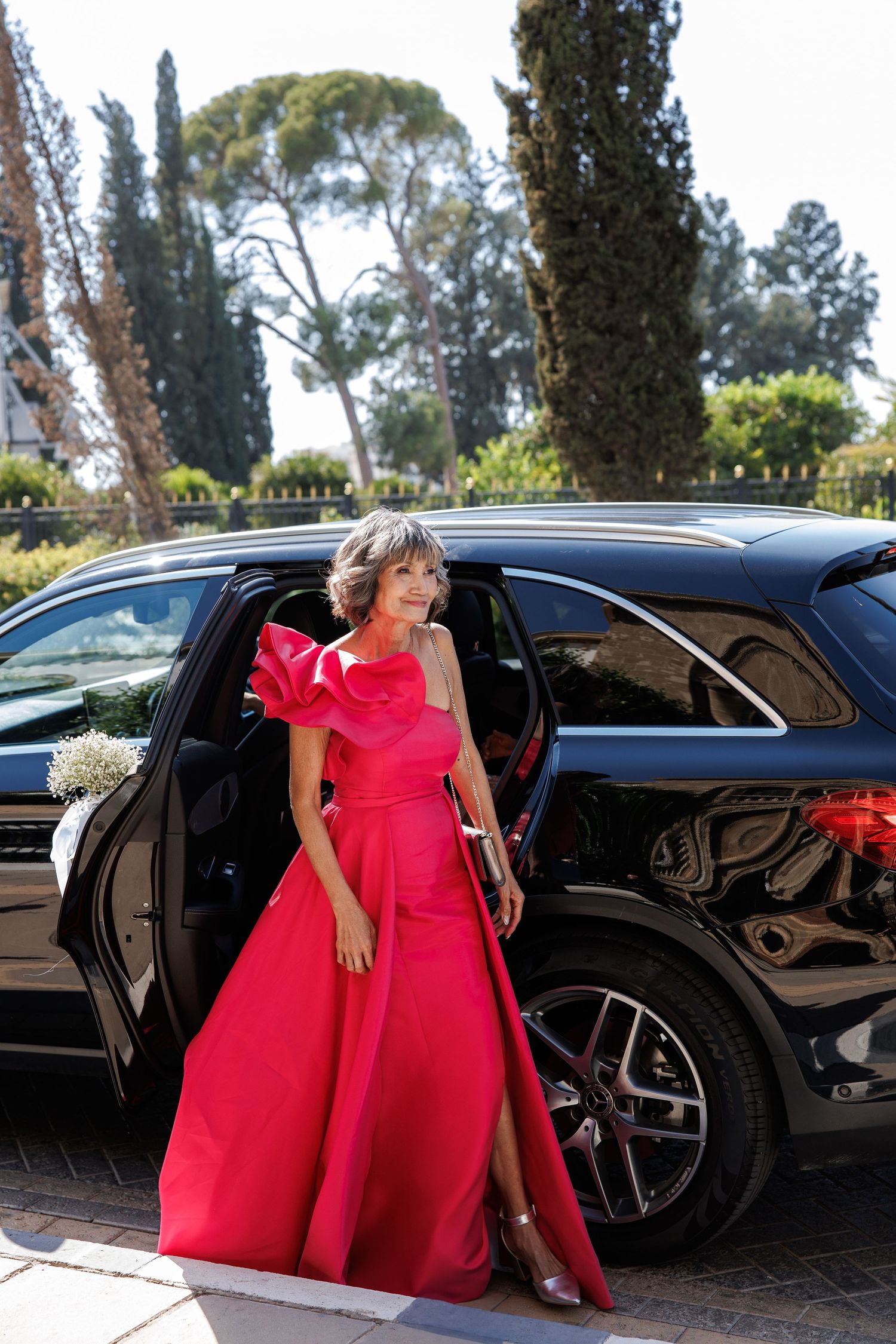 Elegant woman in a red gown stepping out of a black luxury SUV at a formal event.