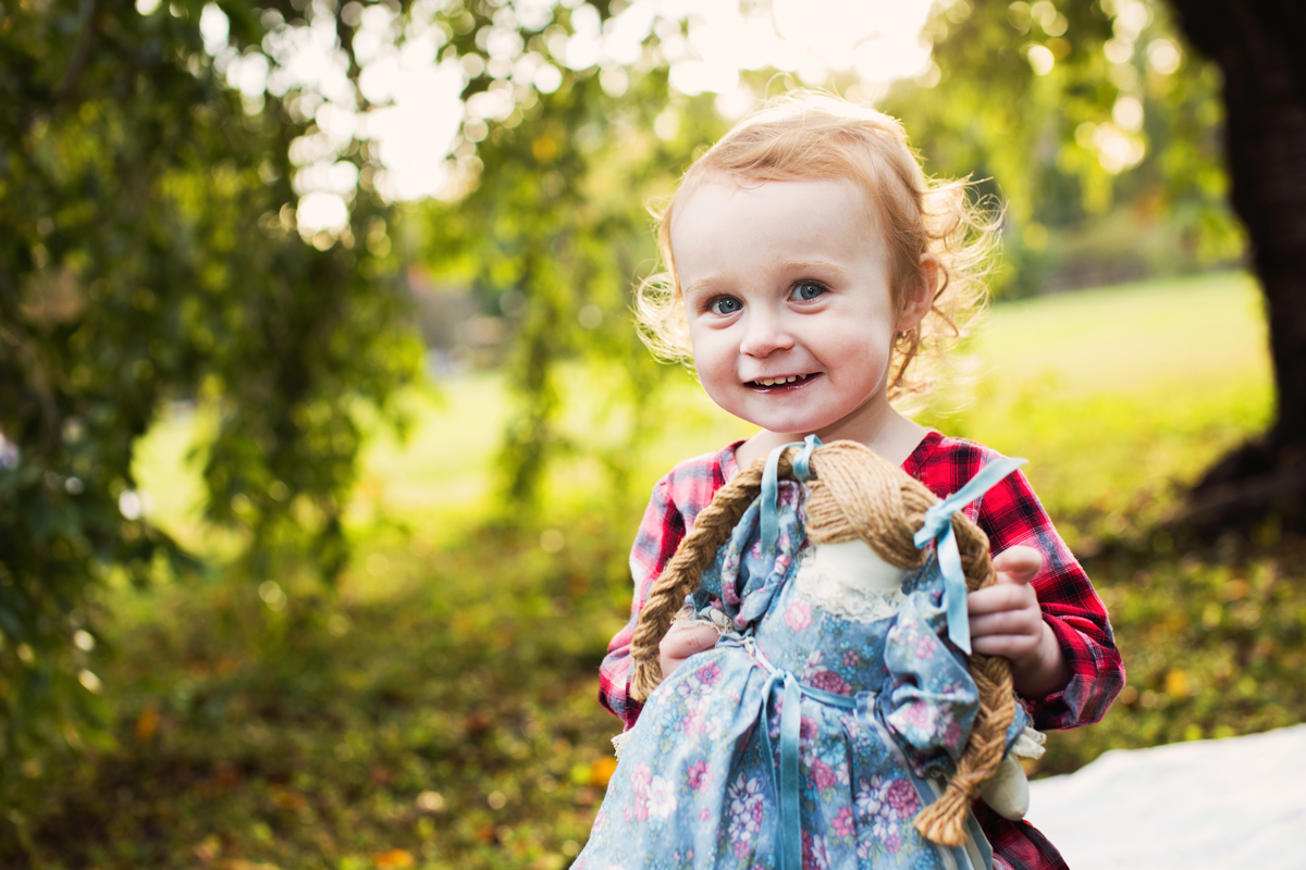 A joyful toddler holds a stuffed toy while playing outside.