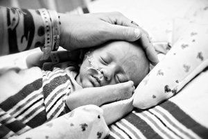 Black and white image of gentle hands cradling a sleeping newborn.