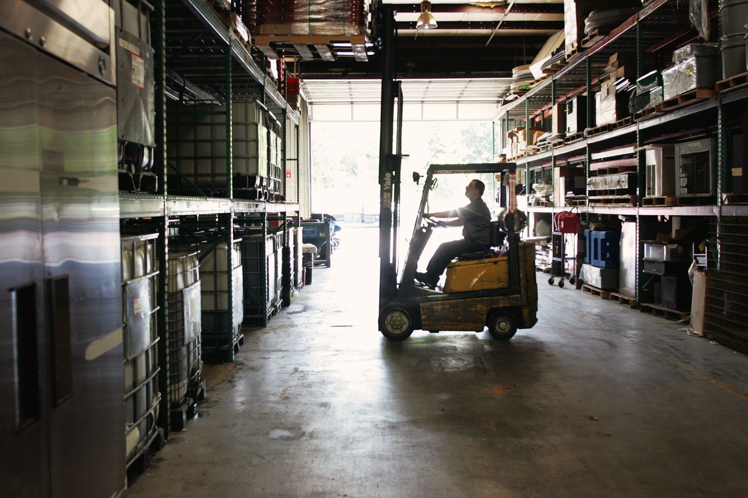 Forklift operator navigating through warehouse storage area with tall shelving units.