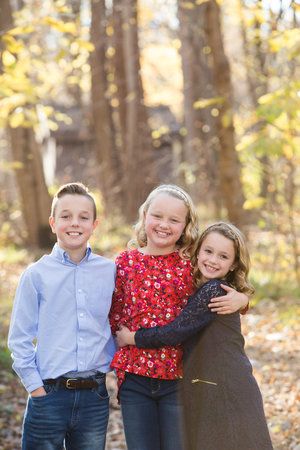 Three happy children pose together for a portrait in an autumn forest setting.