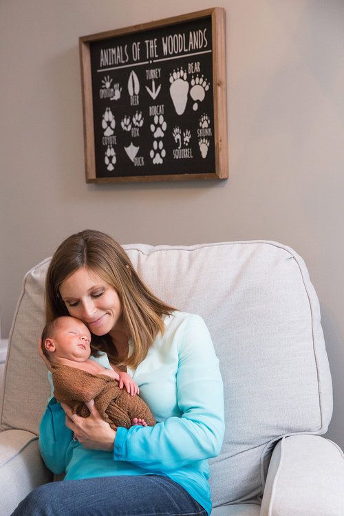 Parent cuddling newborn baby on couch beneath woodland animal print wall art.